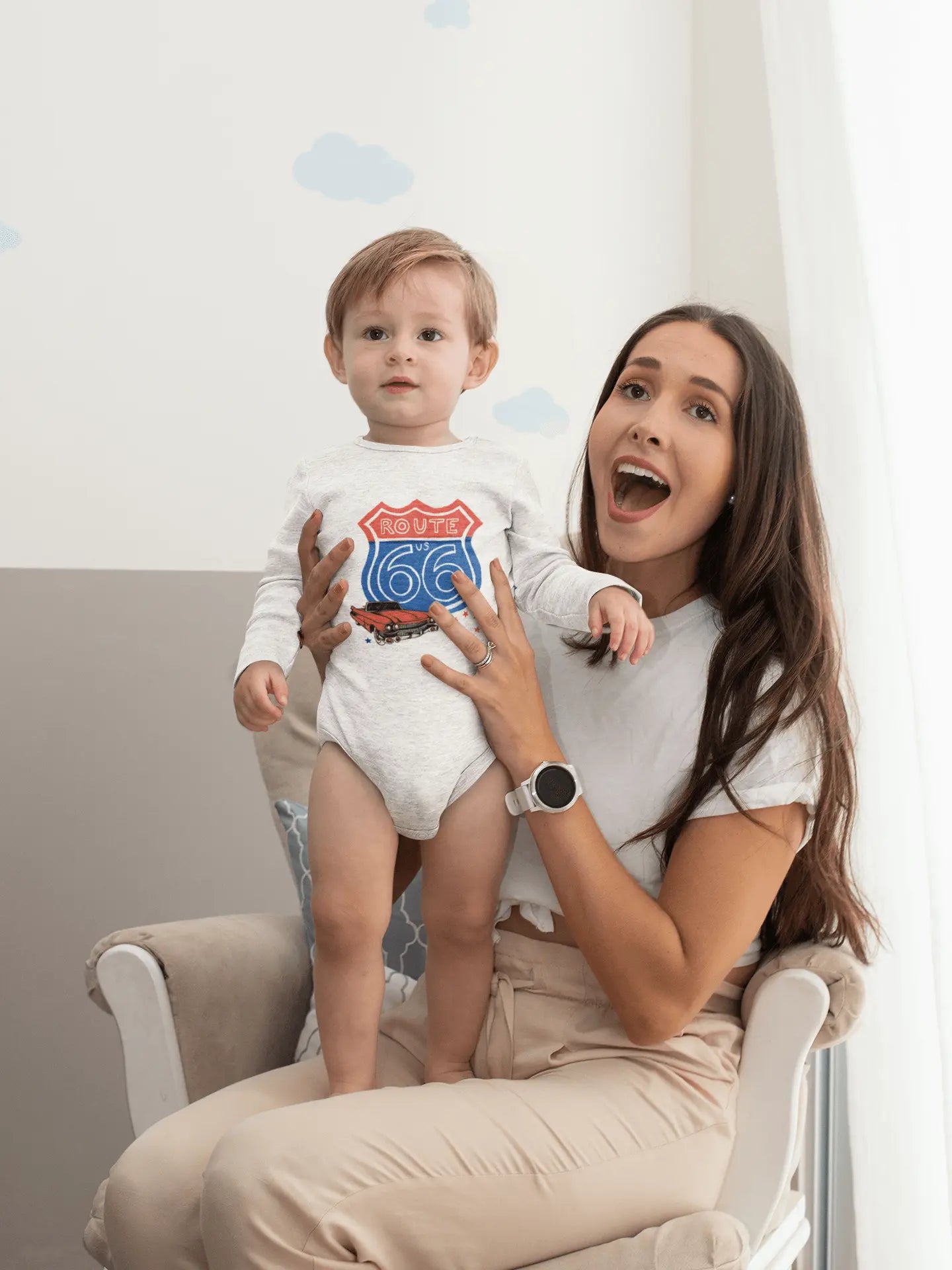 Mother holding her baby who is wearing a Route 66 infant bodysuit with the shield and a red convertible design. It is a vintage road trip inspired outfit and it's perfect for Route 66 baby shower gifts or family travel photos.