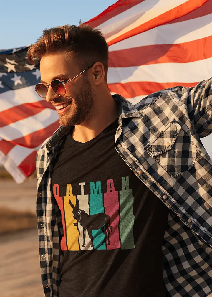 Man in sunglasses and draped in the U.S. flag is wearing a black Oatman t-shirt with the text "Oatman" and a donkey against multicolored backdrop.