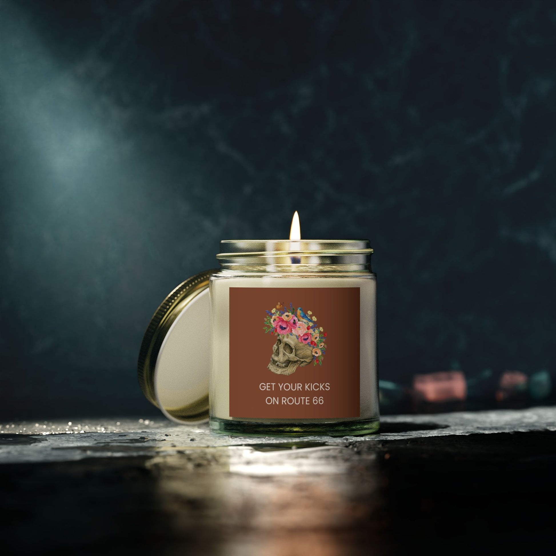 Floral skull Route 66 clear jar candle lit on dark textured surface, moody gothic ambiance