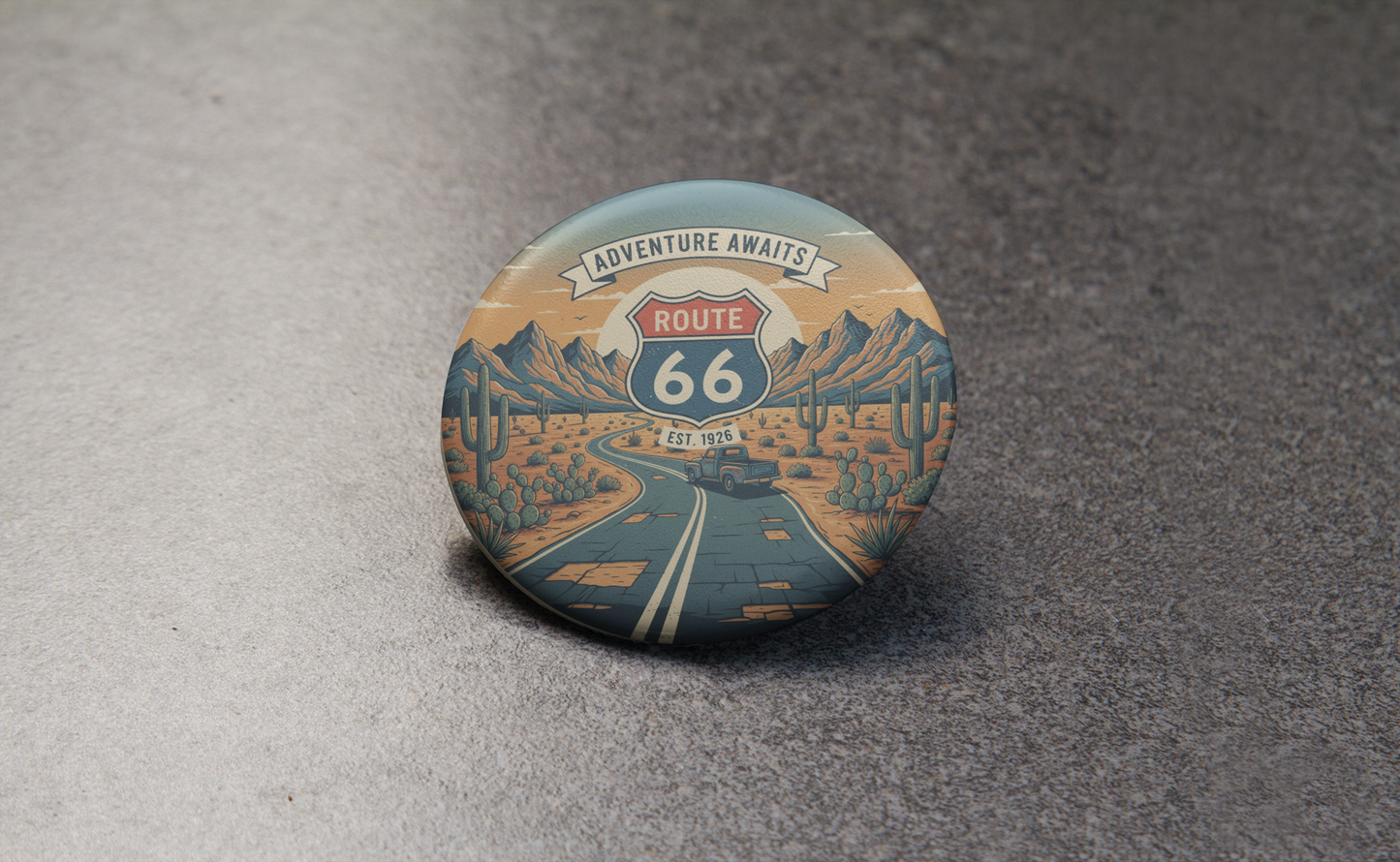 Close-up of Route 66 'Adventure Awaits' pin button featuring a retro desert Route 66 scene.
