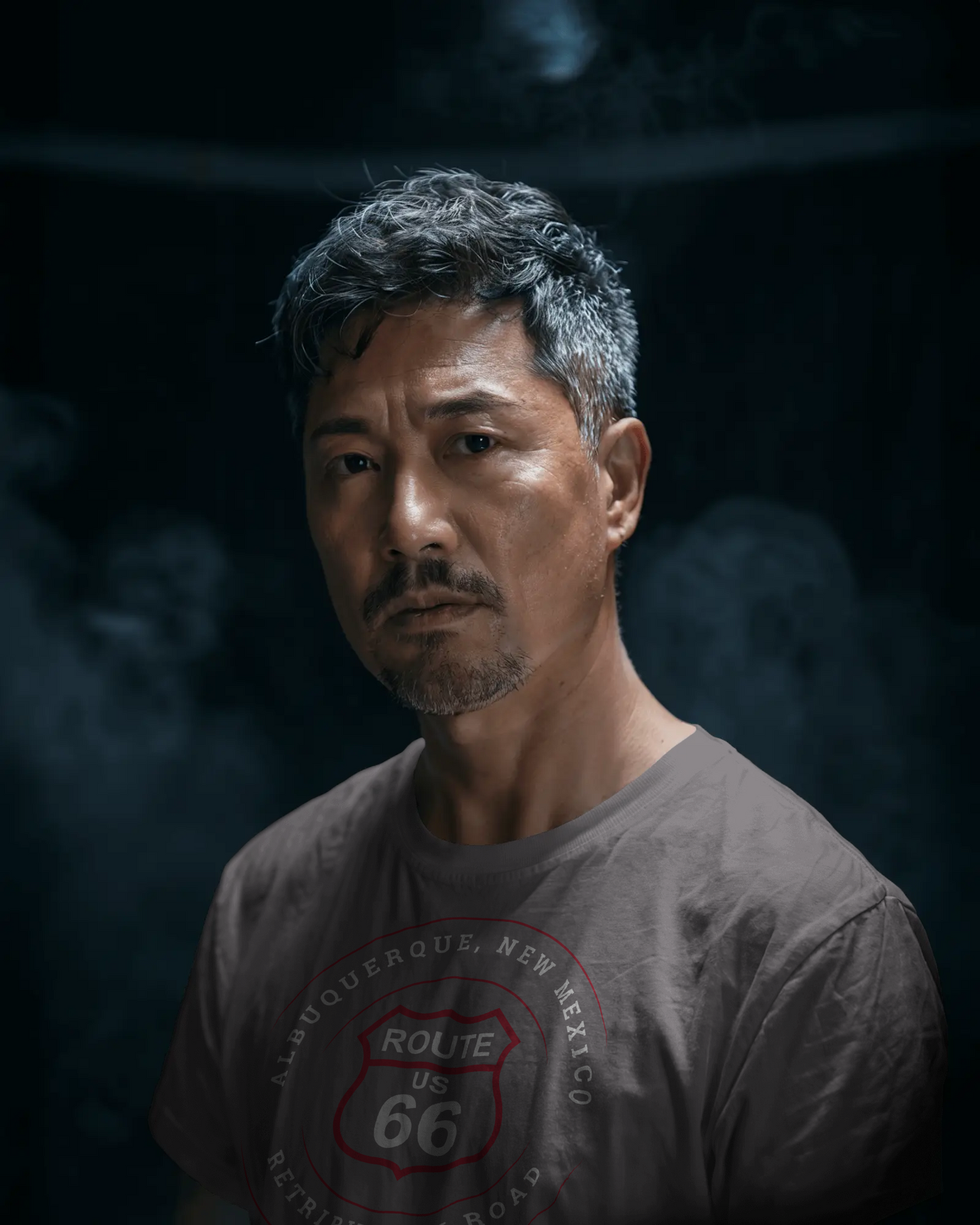 Male model wearing dark grey heather retro Route 66 unisex jersey tee with Albuquerque, NM: "Retribution Road" design with smoke in the background