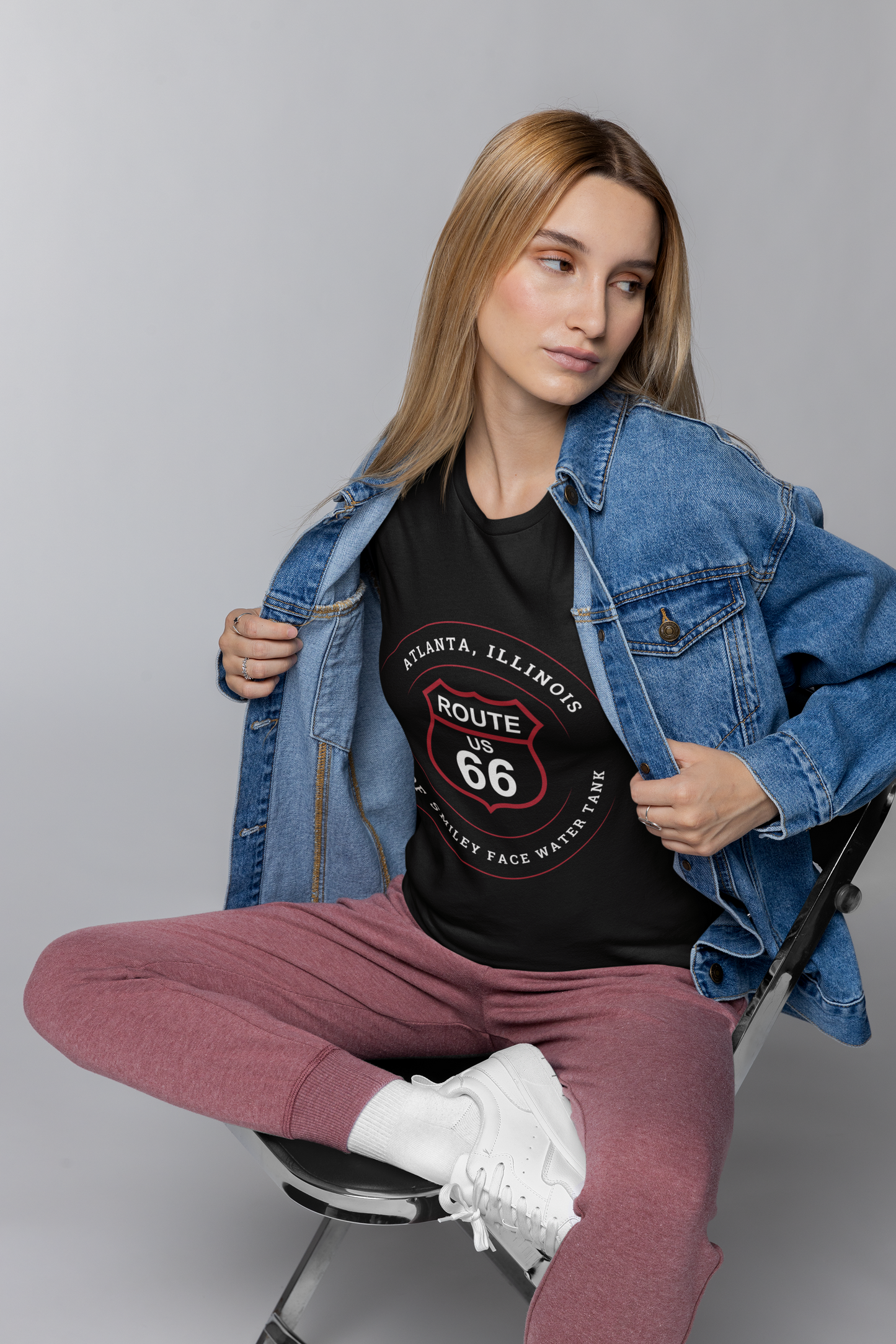 Female model wearing a black retro Route 66 unisex jersey tee with a Atlanta, IL:: "Home of Smiley Face Water Tank" design
