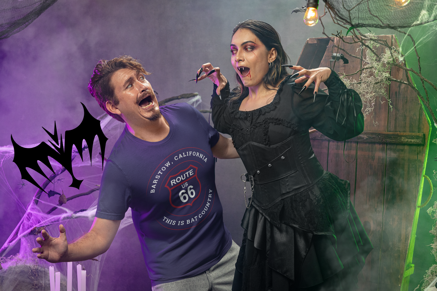 A female dressed in a terrifying bat outfit extends her claws and frightens male model wearing team navy retro Route 66 unisex jersey tee with Barstow, CA: "This is Bat Country" design