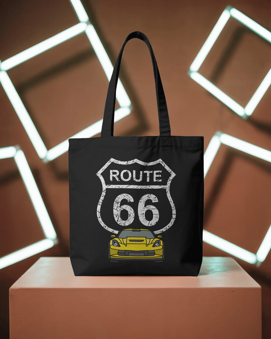 Black Route 66 tote bag with a vintage yellow car graphic, displayed on pedestal with modern geometric neon lights in the background.