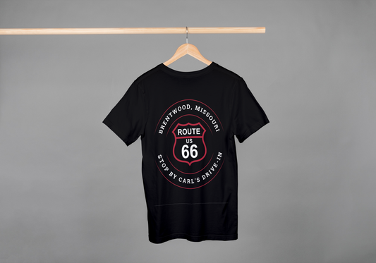 A black retro Route 66 unisex jersey tee with a Brentwood, MO: "Stop By Carl's Drive-In" design hanging off a wooden hanger on a pole