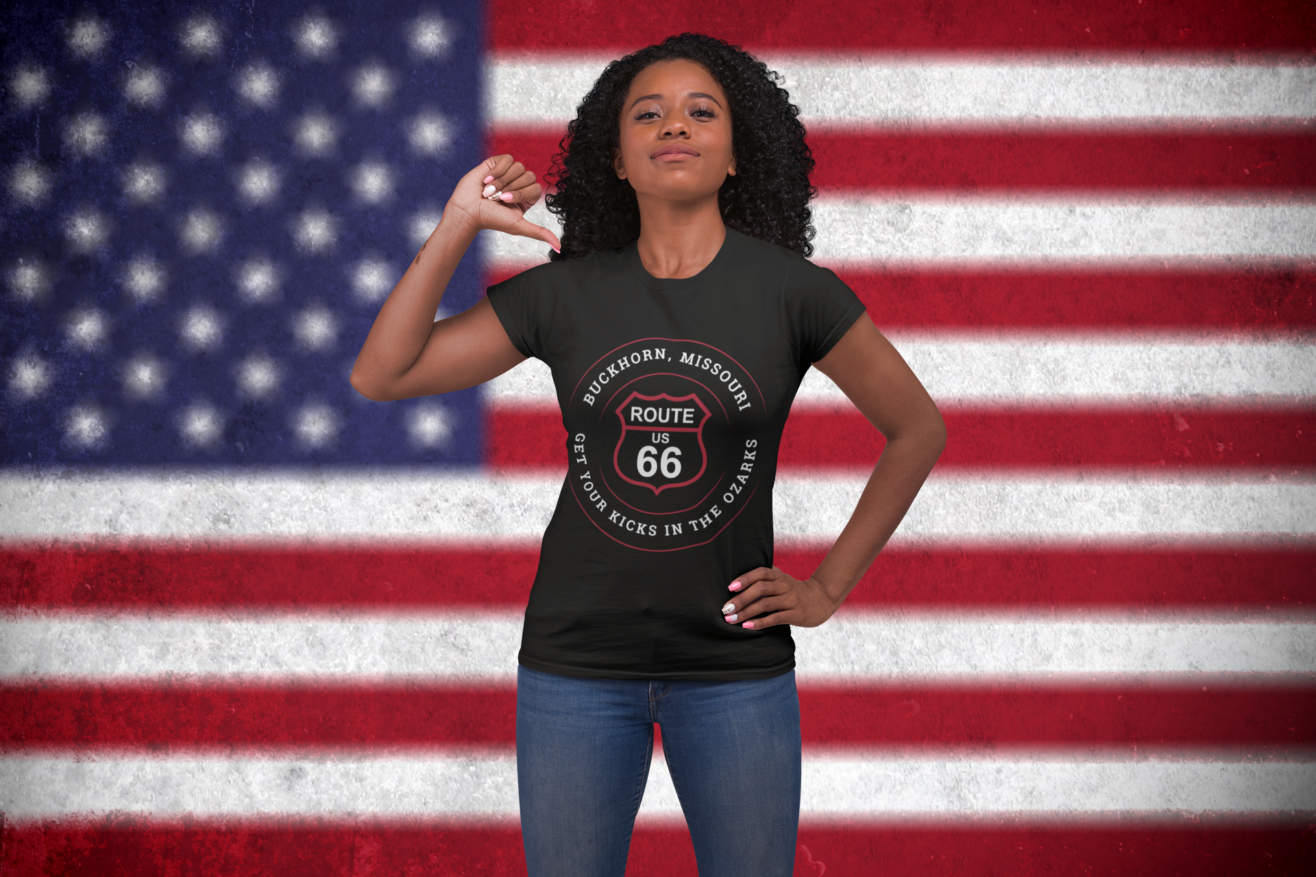 Female model wearing a black retro Route 66 unisex jersey tee with a Buckhorn, MO: "Get Your Kicks in the Ozarks" design with a USA flag background