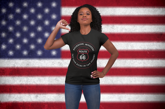 Female model wearing a black retro Route 66 unisex jersey tee with a Buckhorn, MO: "Get Your Kicks in the Ozarks" design with a USA flag background