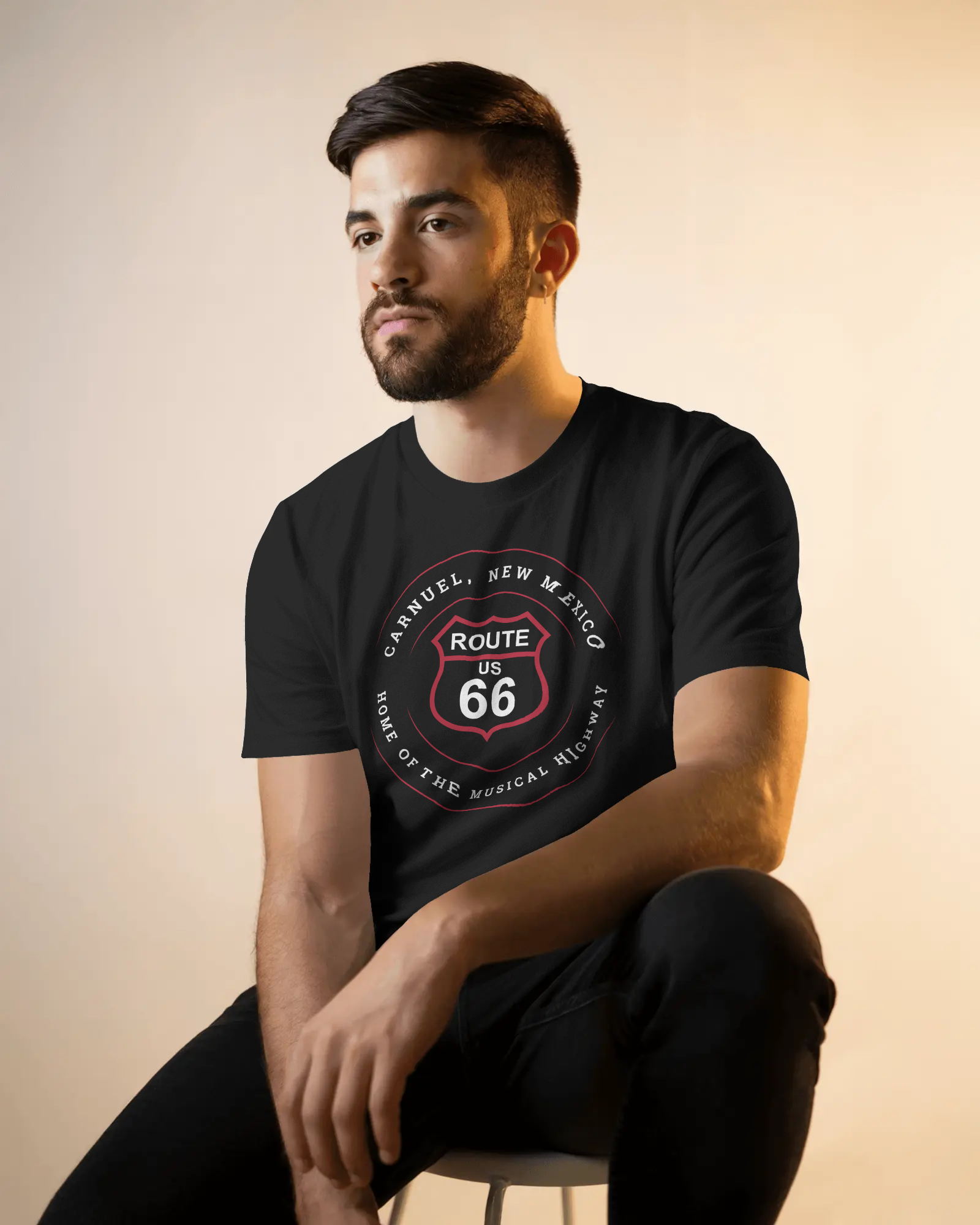 Male model wearing black retro Route 66 unisex jersey tee with Carnuel, NM: Home of the Musical Highway graphic
