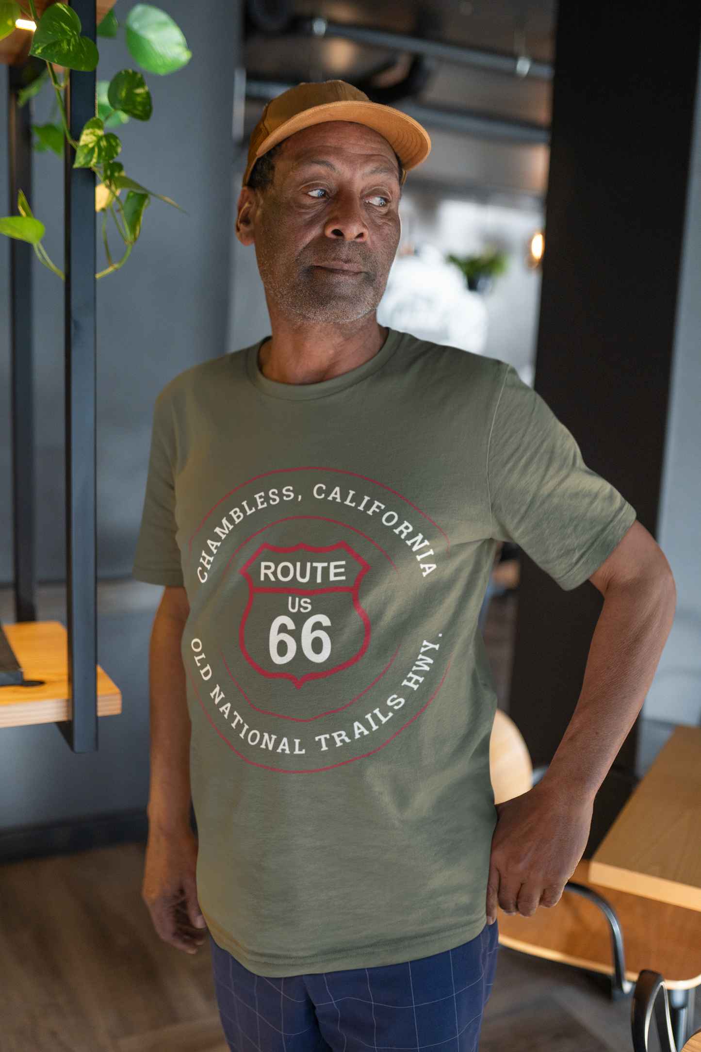 Male model wearing a tan baseball cap and a heather military green retro Route 66 unisex jersey tee with Chambless, CA: "Old National Trails Hwy" design