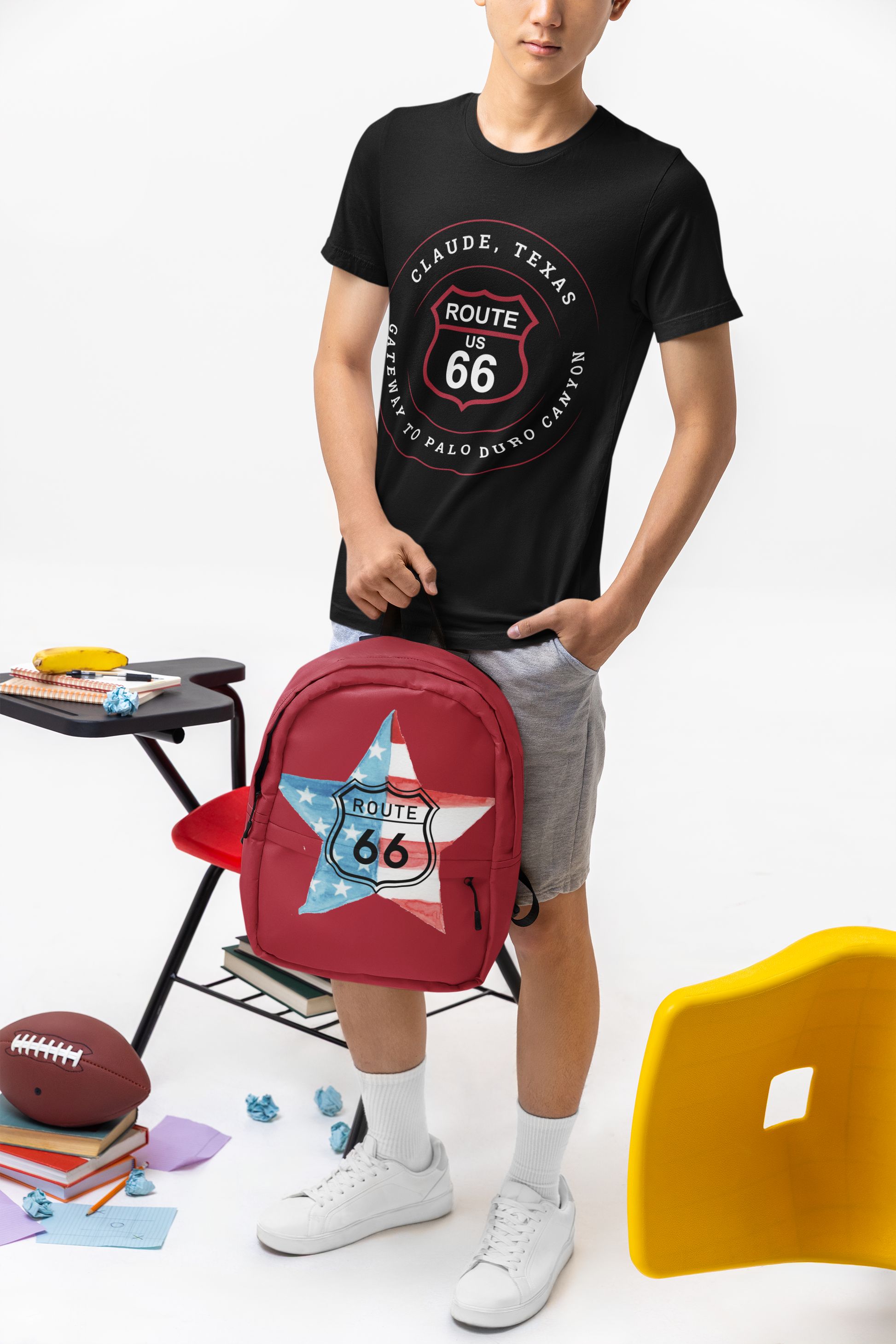 Male model wearing a black retro Route 66 unisex jersey tee with Claude, TX: "Gateway to Palo Duro Canyon" design and holding a red school backpack with a Route 66 star-shaped US flag logo