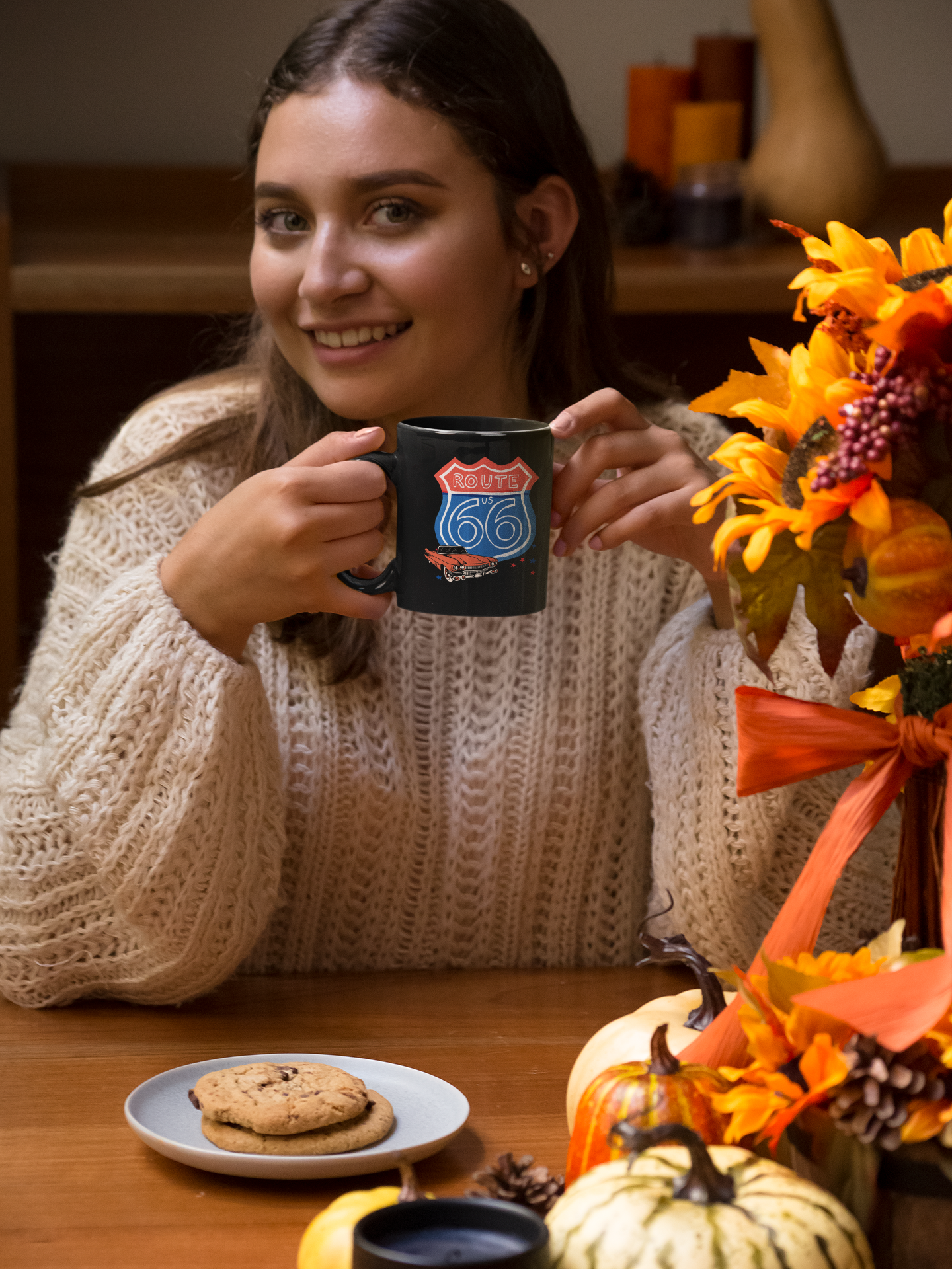 Smiling woman enjoying coffee from a Route 66 Corvette latte mug at a cozy autumn table with pumpkins and cookies