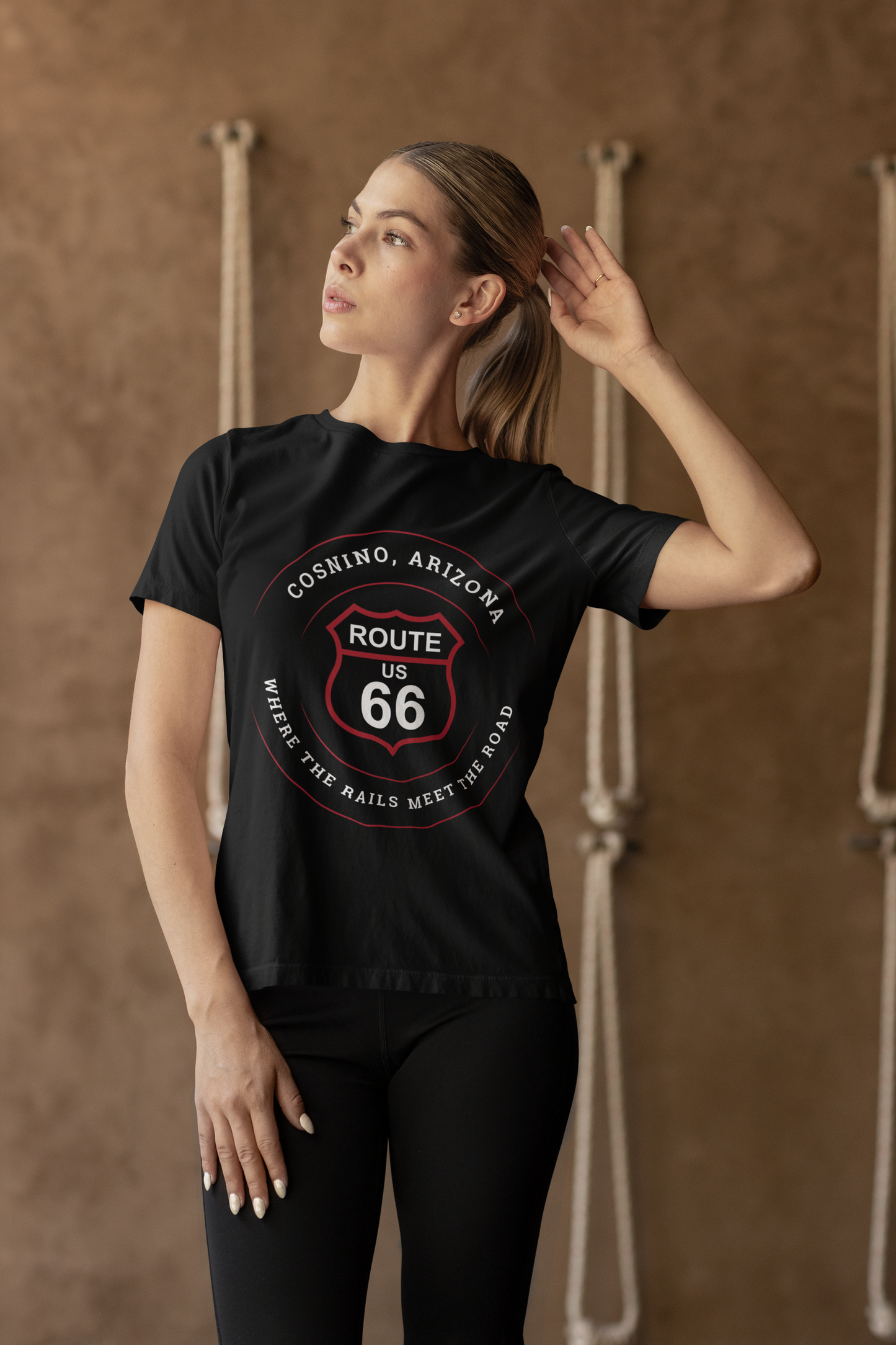 Female model wearing a black retro Route 66 unisex jersey tee with a Cosnino, AZ: "Where the Rail Meets the Road" design