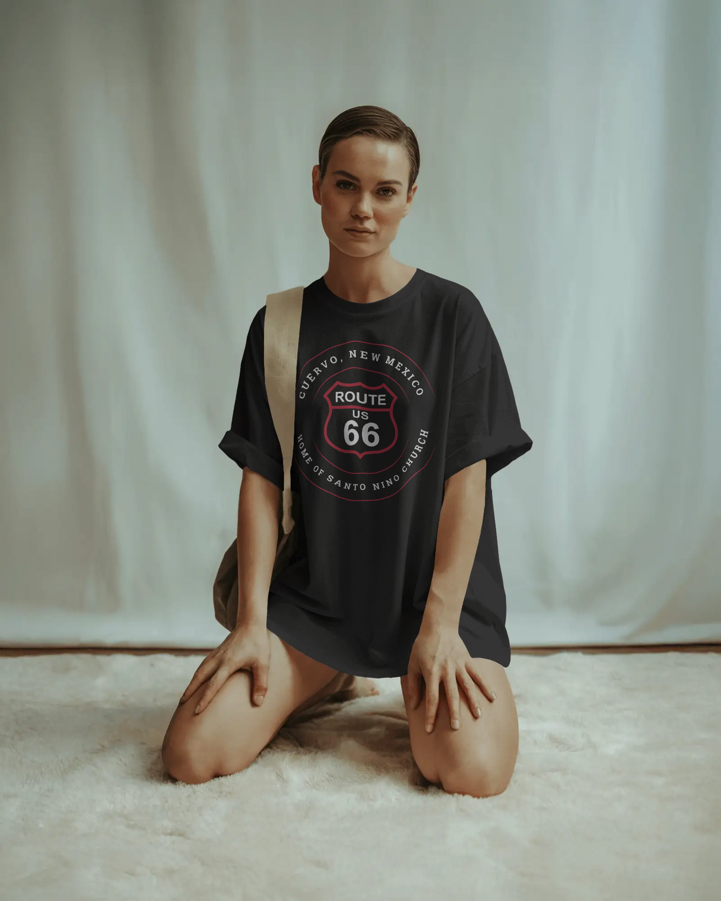 Female model wearing black retro Route 66 unisex jersey tee with Cuervo, NM: Home of Santo Niño Church graphic