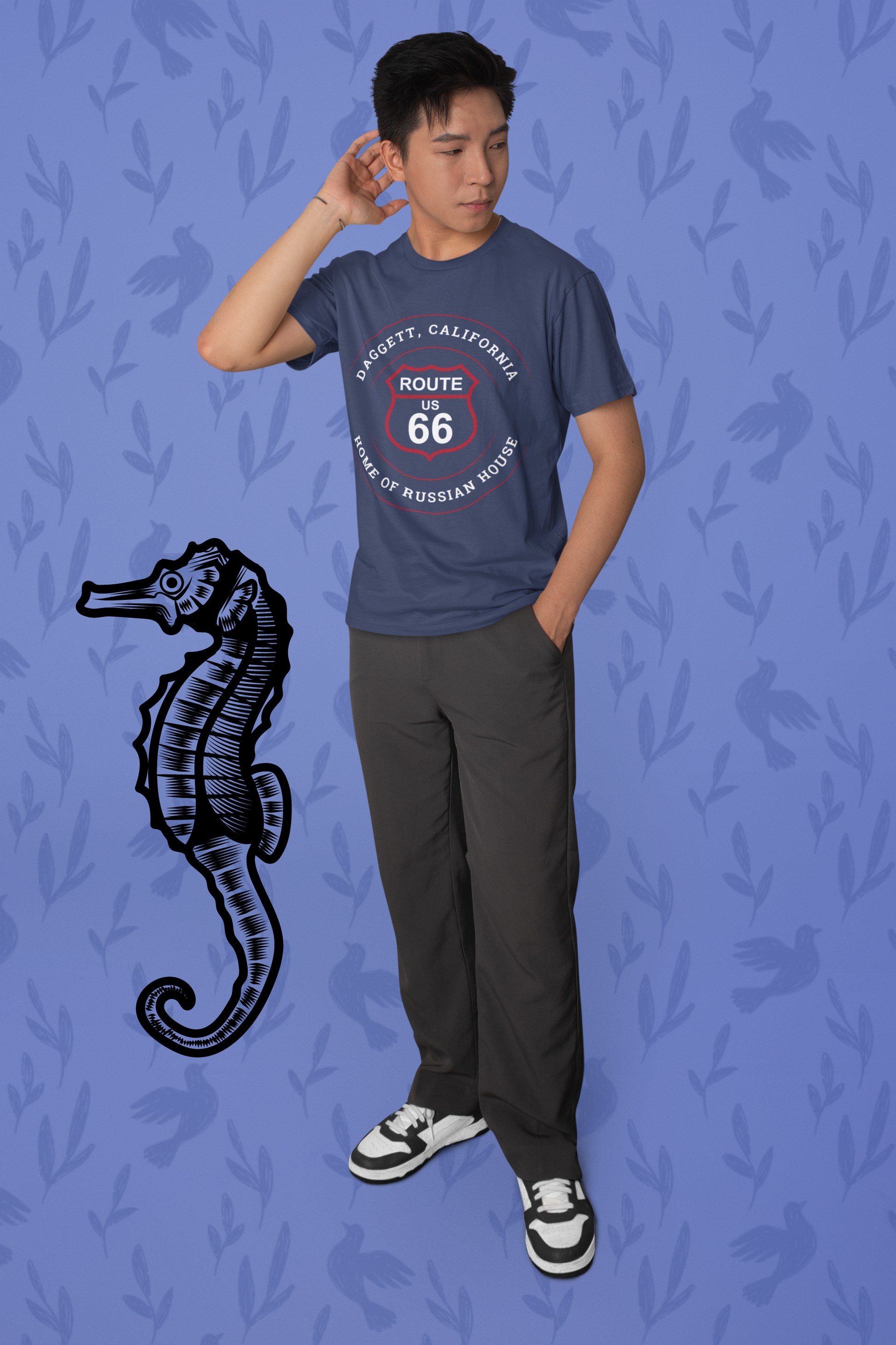 Male model wearing heather navy retro Route 66 unisex jersey tee with Daggett, CA: "Home of Russian House" design and standing next to a seahorse graphic