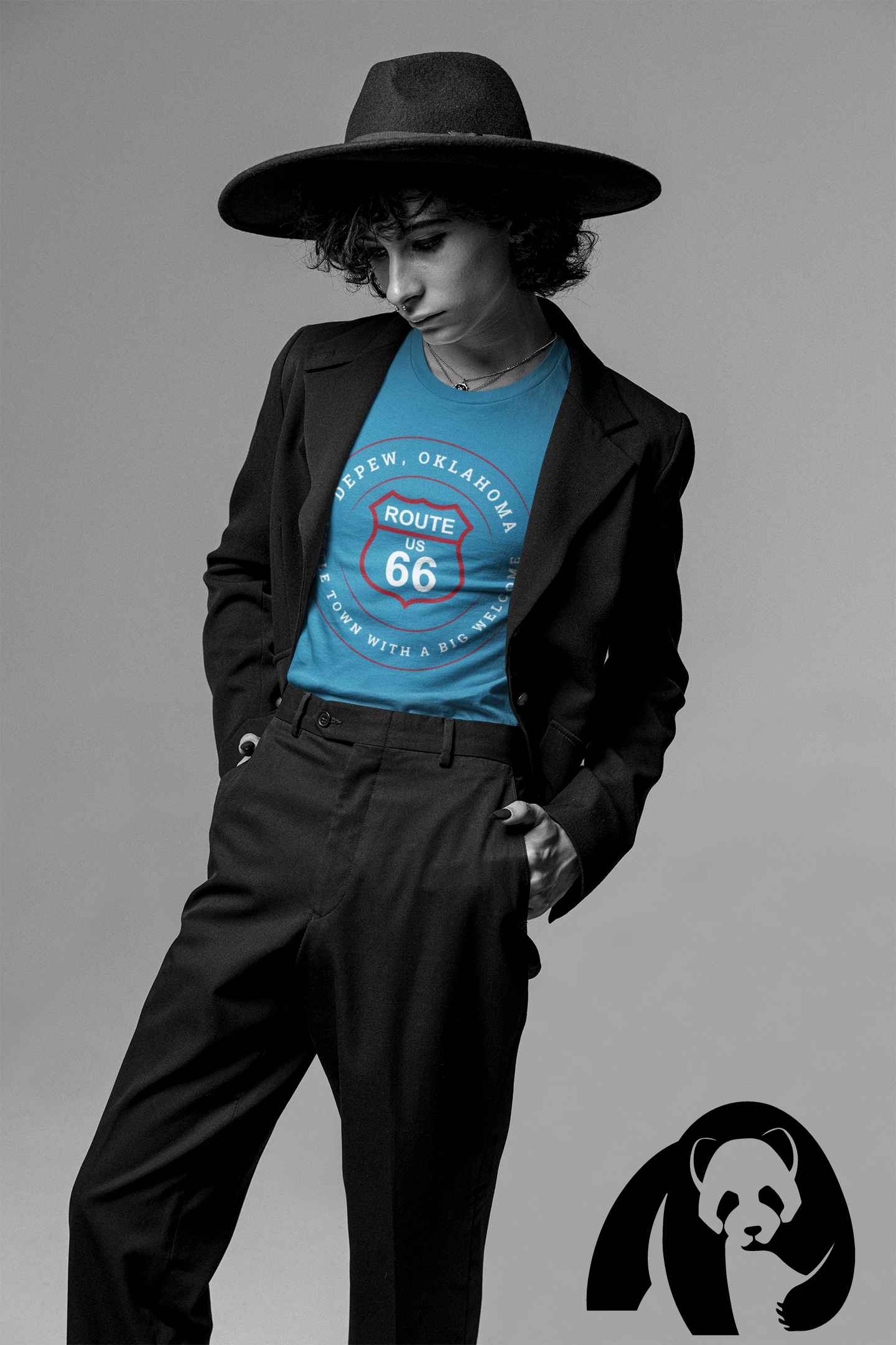 Model in wide-brim black hat and suit jacket wearing an aqua retro Route 66 unisex jersey tee with Depew, OK: "Little Town with a Big Welcome" graphic, posing against a gray background.