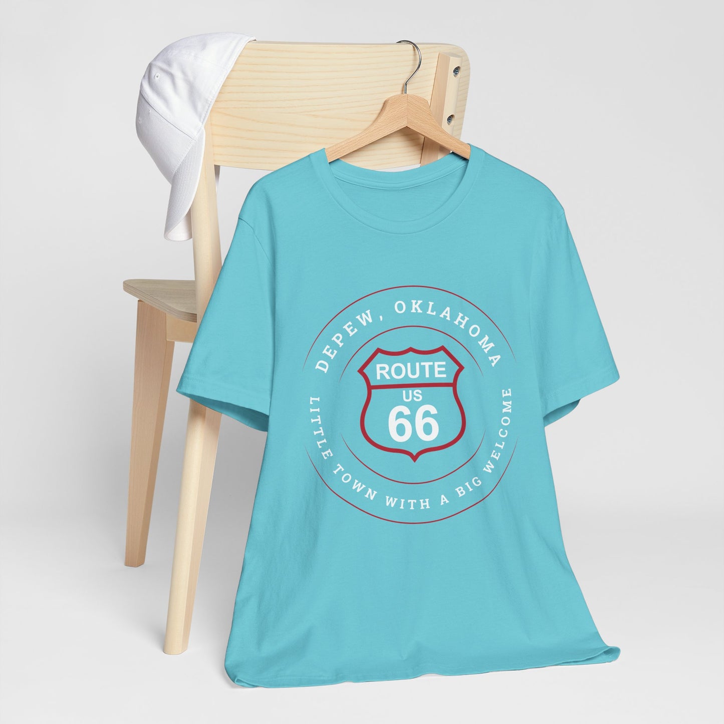 Turquoise retro Route 66 unisex jersey tee with Depew, OK "Little Town with a Big Welcome" design hanging on a wooden hanger and hanging off a wooden chair
