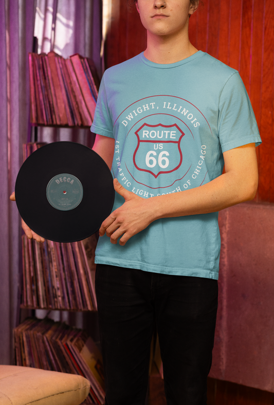 A man models a turquoise retro Route 66 unisex jersey tee with a Dwight, IL: "1st Traffic Light South of Chicago" design, while also proudly holding a Rolling Stones' Route 66 vinyl album.