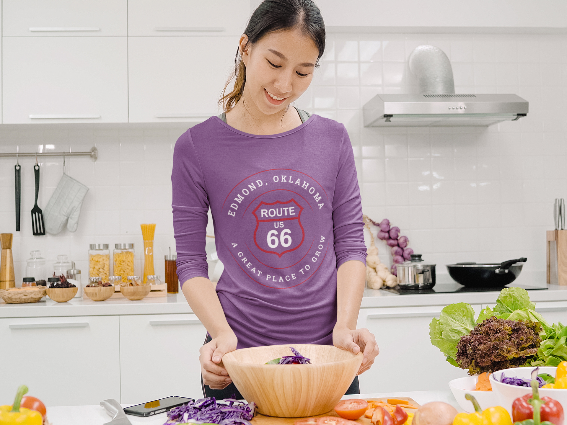 Female model in the kitchen cooking and wearing a heather team purple retro Route 66 unisex jersey tee with Edmond, OK "A Great Place to Grow" design