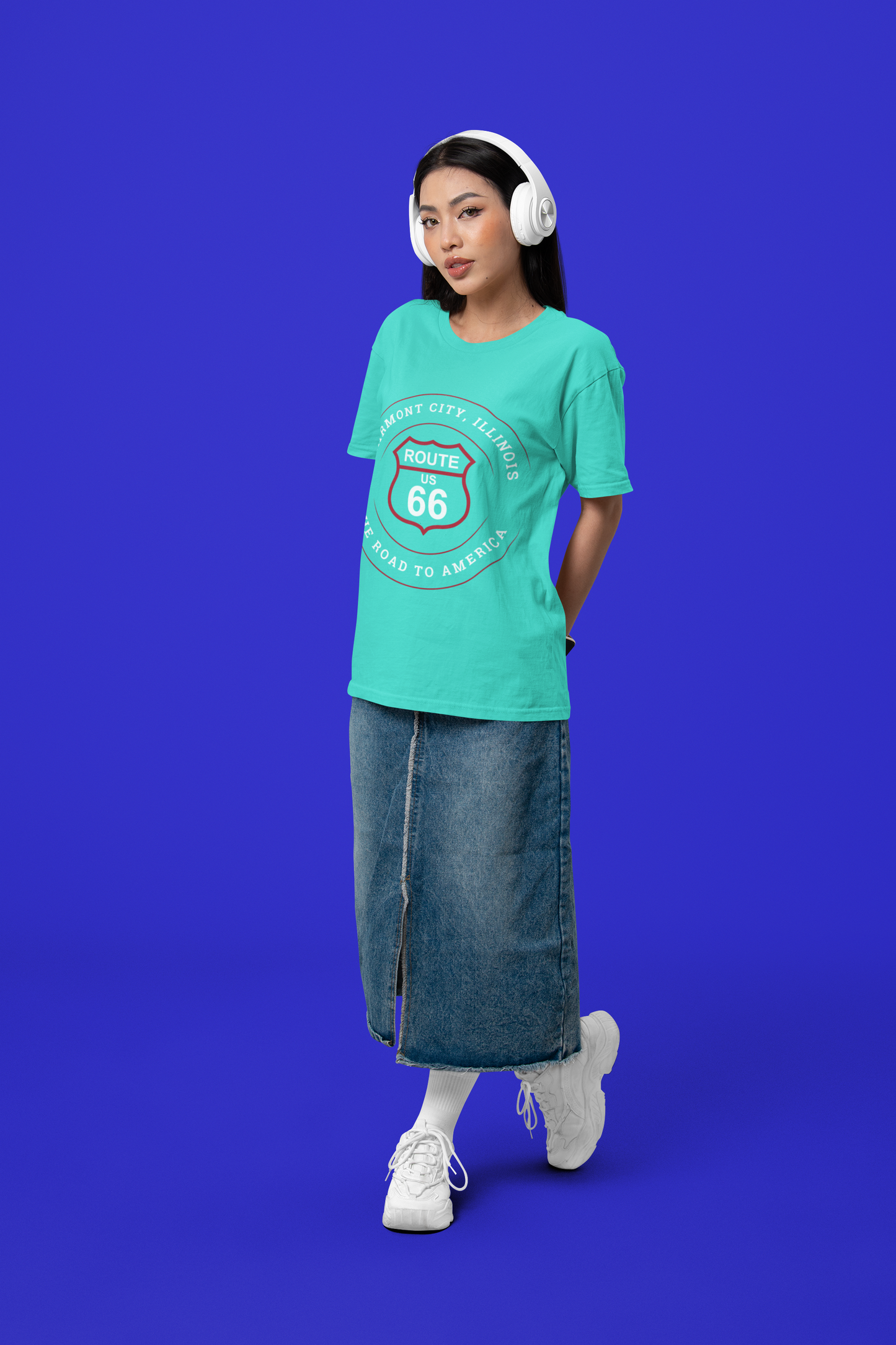 Female model wearing a turquoise retro Route 66 unisex jersey tee with a Fairmount City, IL:: "The Road to America" design