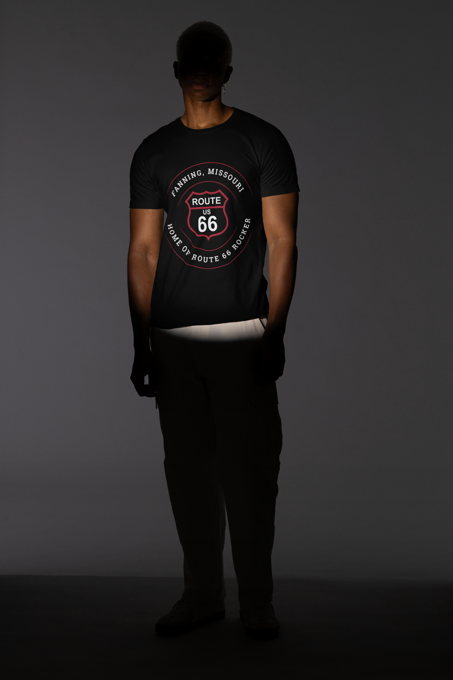 Male model wearing a black retro Route 66 unisex jersey tee with a Fanning, MO: "Home of the Route 66 Rocker" design. His face is covered by a dark shadow
