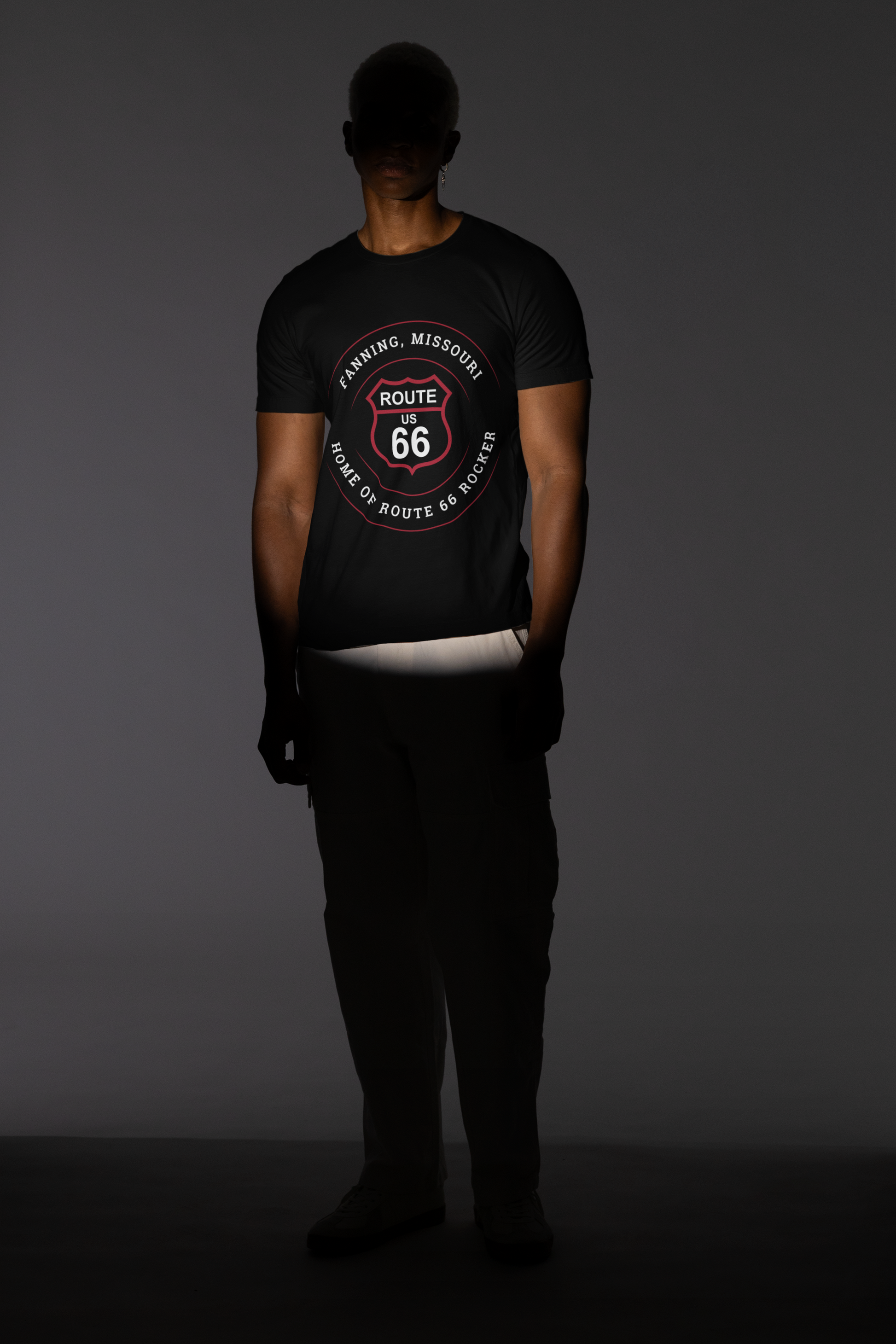 Male model wearing a black retro Route 66 unisex jersey tee with a Fanning, MO: "Home of the Route 66 Rocker" design. His face is covered by a dark shadow