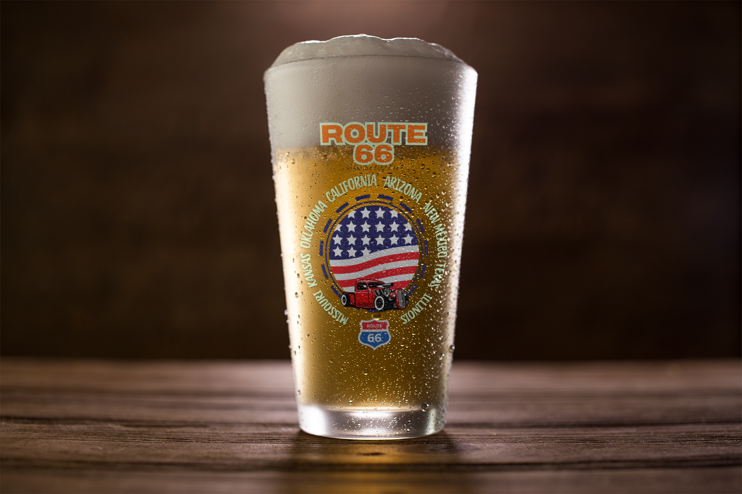 Close-up of Route 66 pint glass filled with beer, featuring a classic red truck and American flag design with all eight Route 66 states listed around the artwork