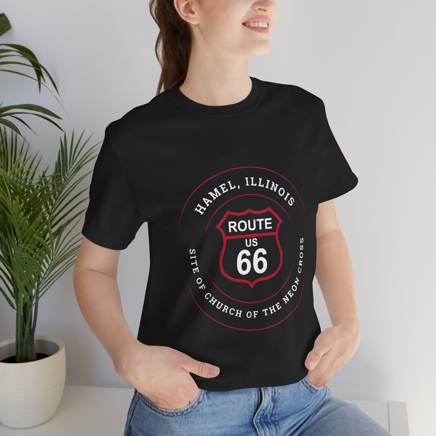 Female model wearing a black retro Route 66 unisex jersey tee with a Hamel, IL:: "Site of the Church of the Neon Cross" design