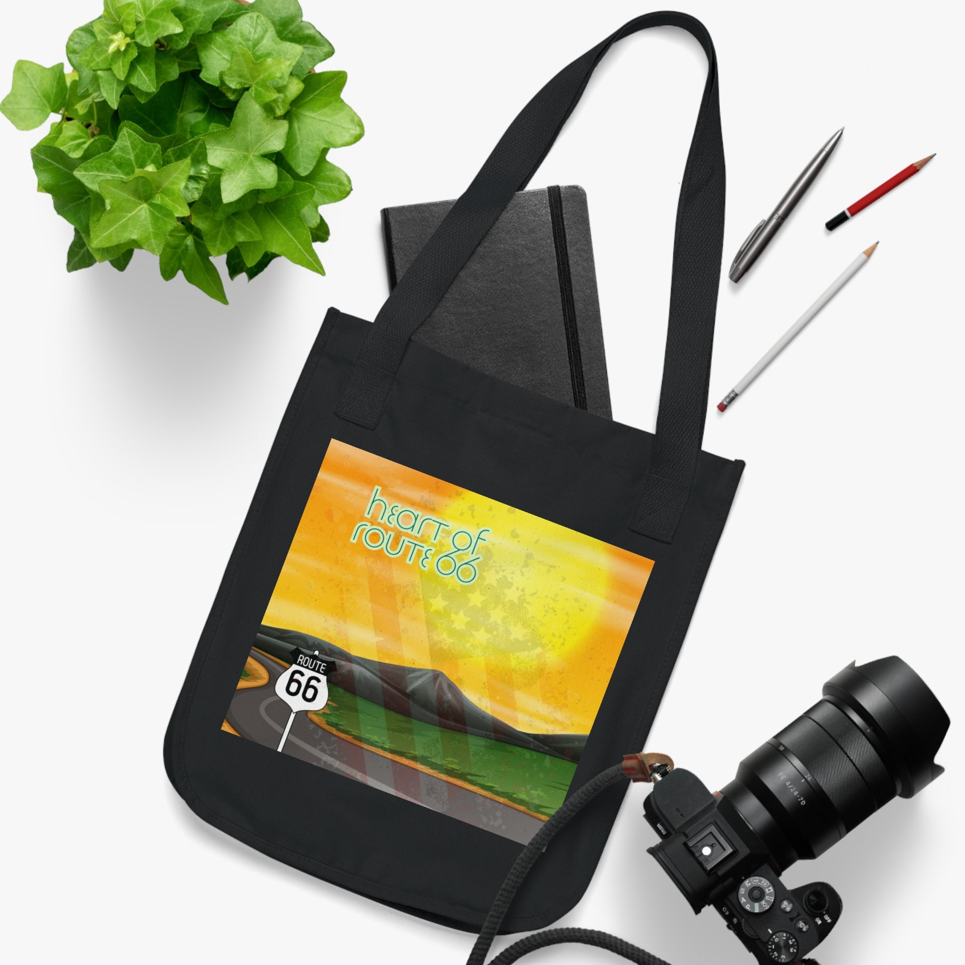 Heart of Route 66 black organic tote bag shown in flat lay with pens, a notebook, a plant and a camera.