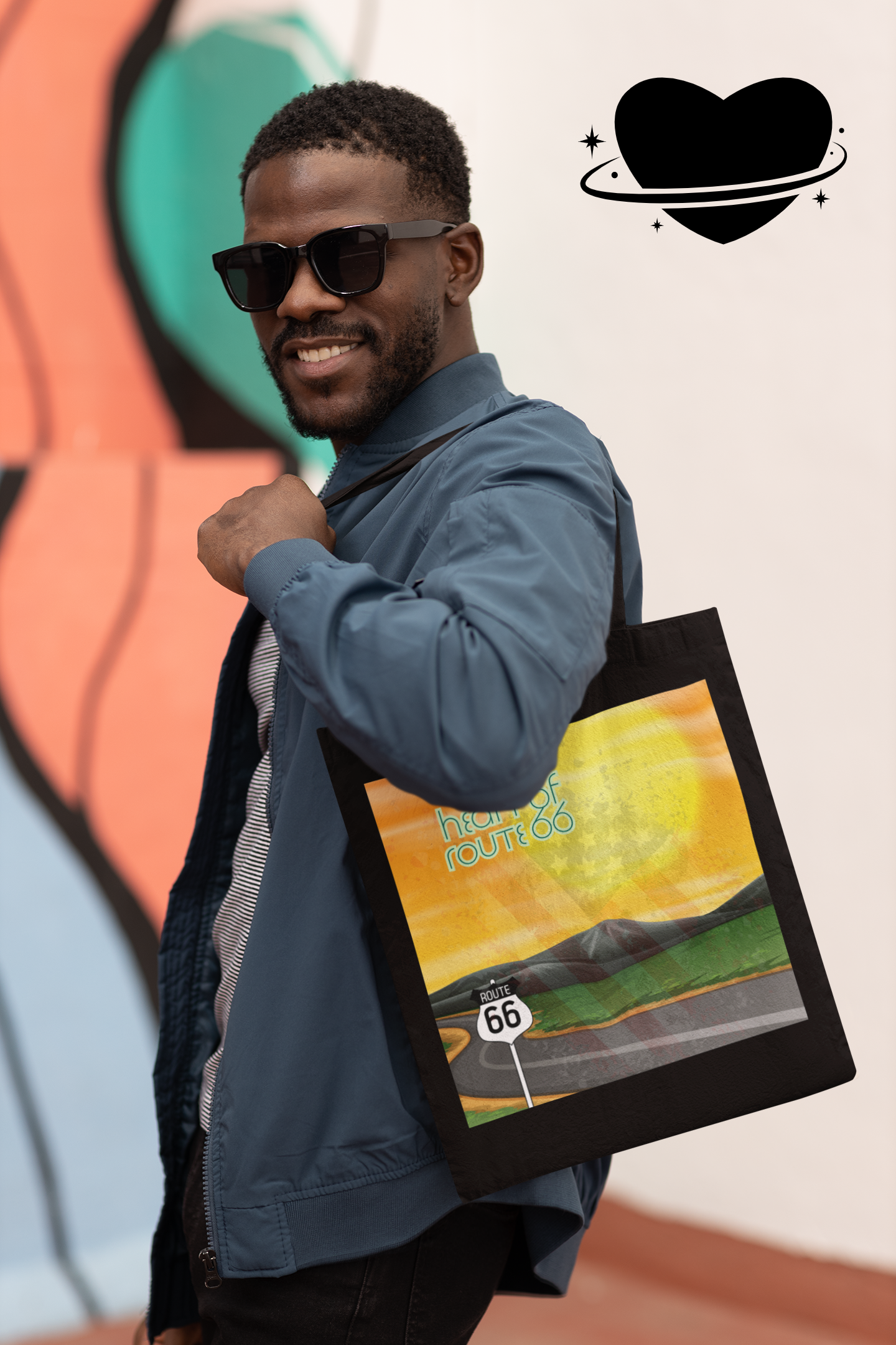 Man wearing sunglasses carrying a black organic Heart of Route 66 tote bag with a desert sunset highway scene.