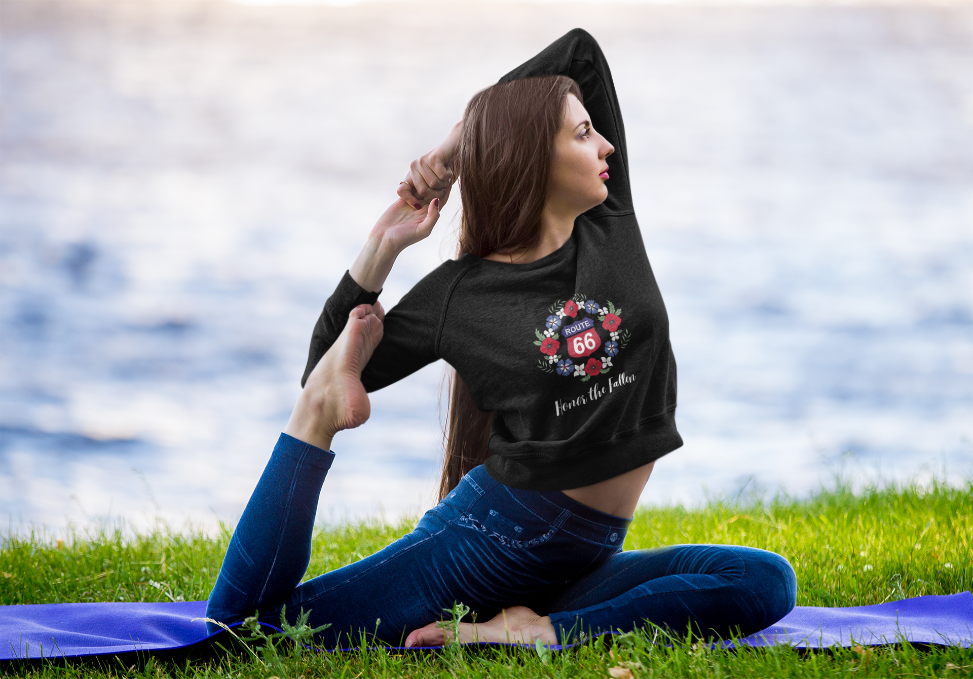 Woman practicing yoga and in One-Legged King Pigeon Pose while wearing a black cropped Route 66 "Honor the Fallen" sweatshirt with a poppy wreath design and a red and blue interstate-styled Route 66 sign
