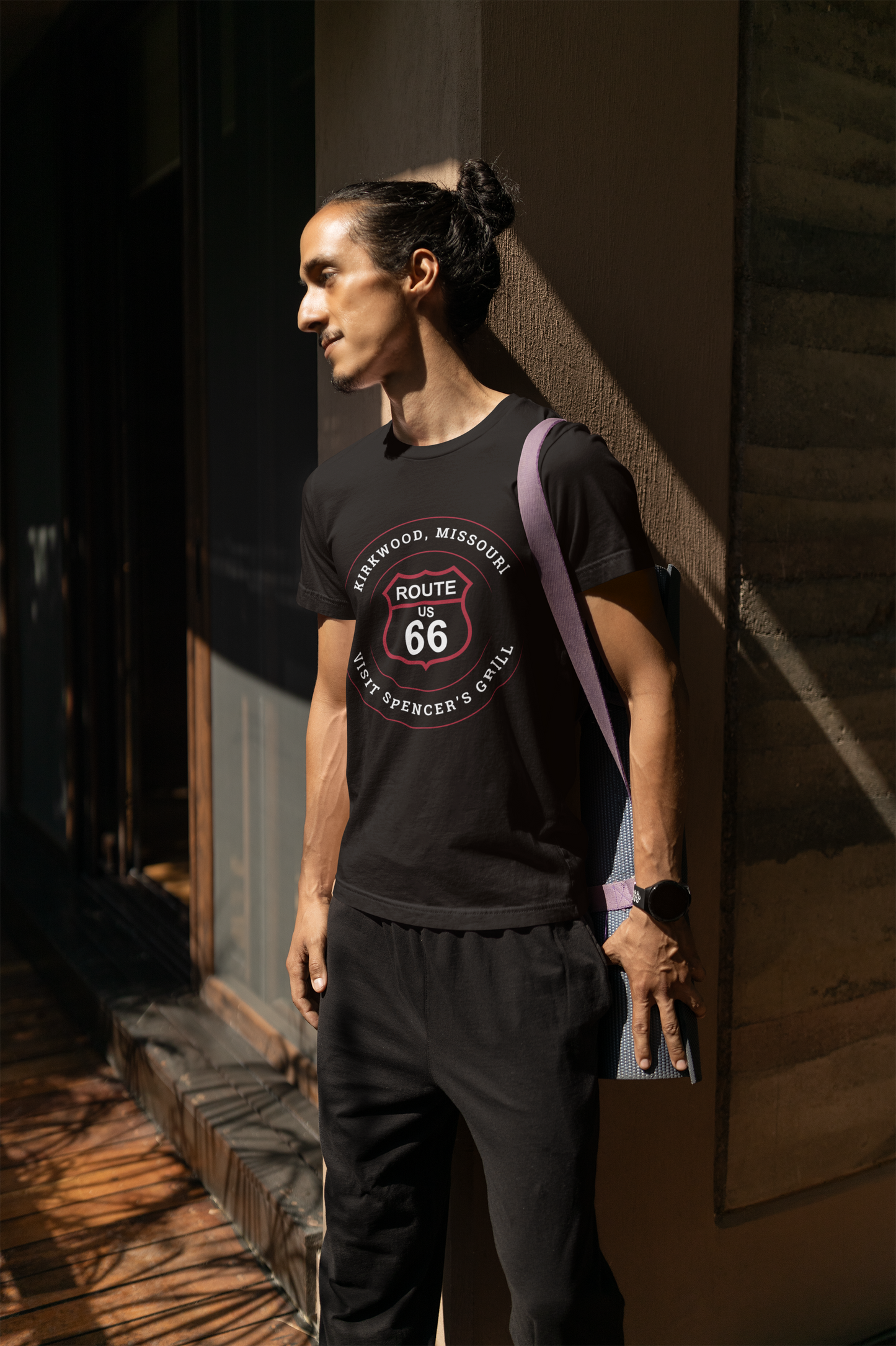 Male model wearing a black retro Route 66 unisex jersey tee with a Kirkwood, MO: "Visit Spencer's Grill" design