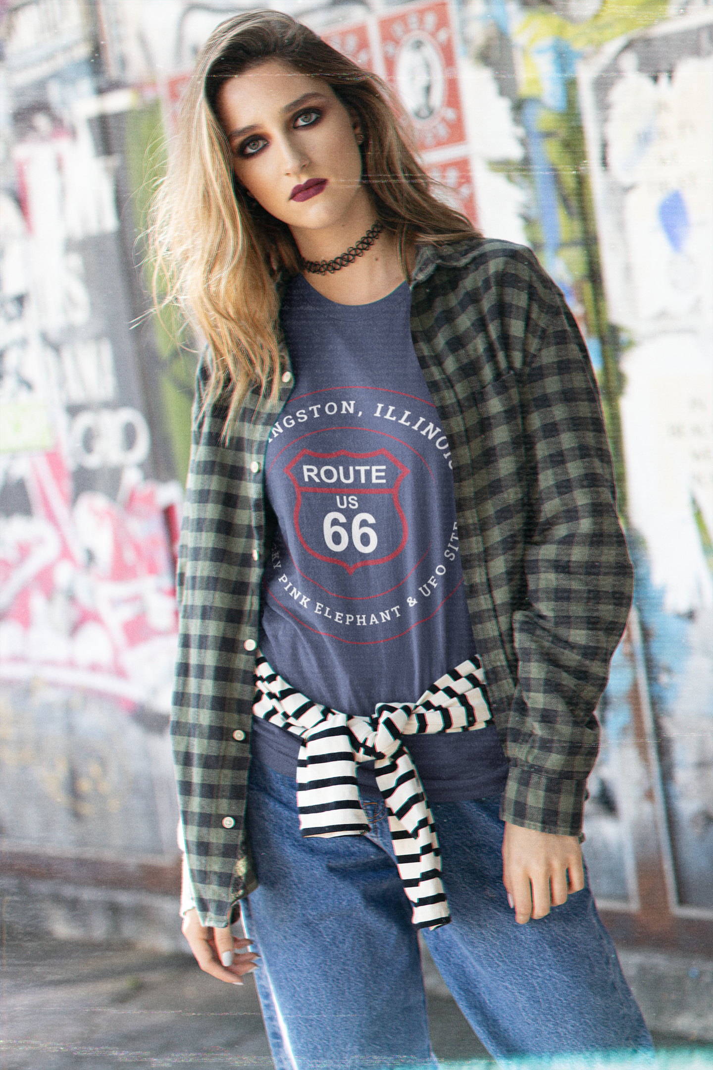 Female model wearing a heather true royal retro Route 66 unisex jersey tee with a Livingston, IL:: "Wacky Pink elephant & UFO Site" design