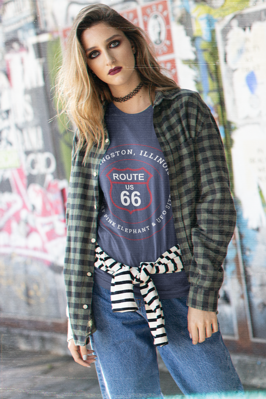 Female model wearing a heather true royal retro Route 66 unisex jersey tee with a Livingston, IL:: "Wacky Pink elephant & UFO Site" design