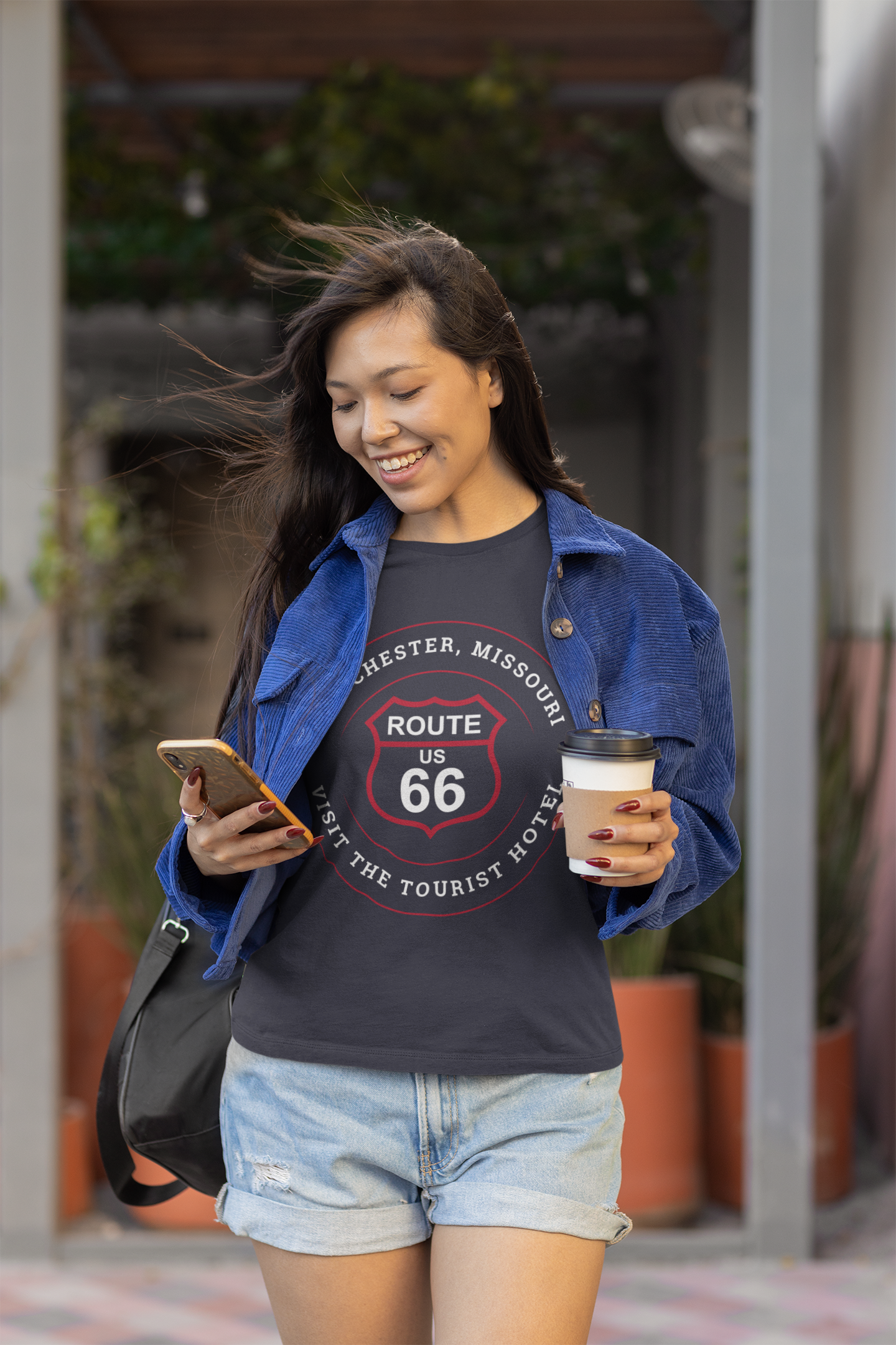 Female model wearing a black heather retro Route 66 unisex jersey tee with a Manchester, MO: "Visit the Tourist Hotel" design