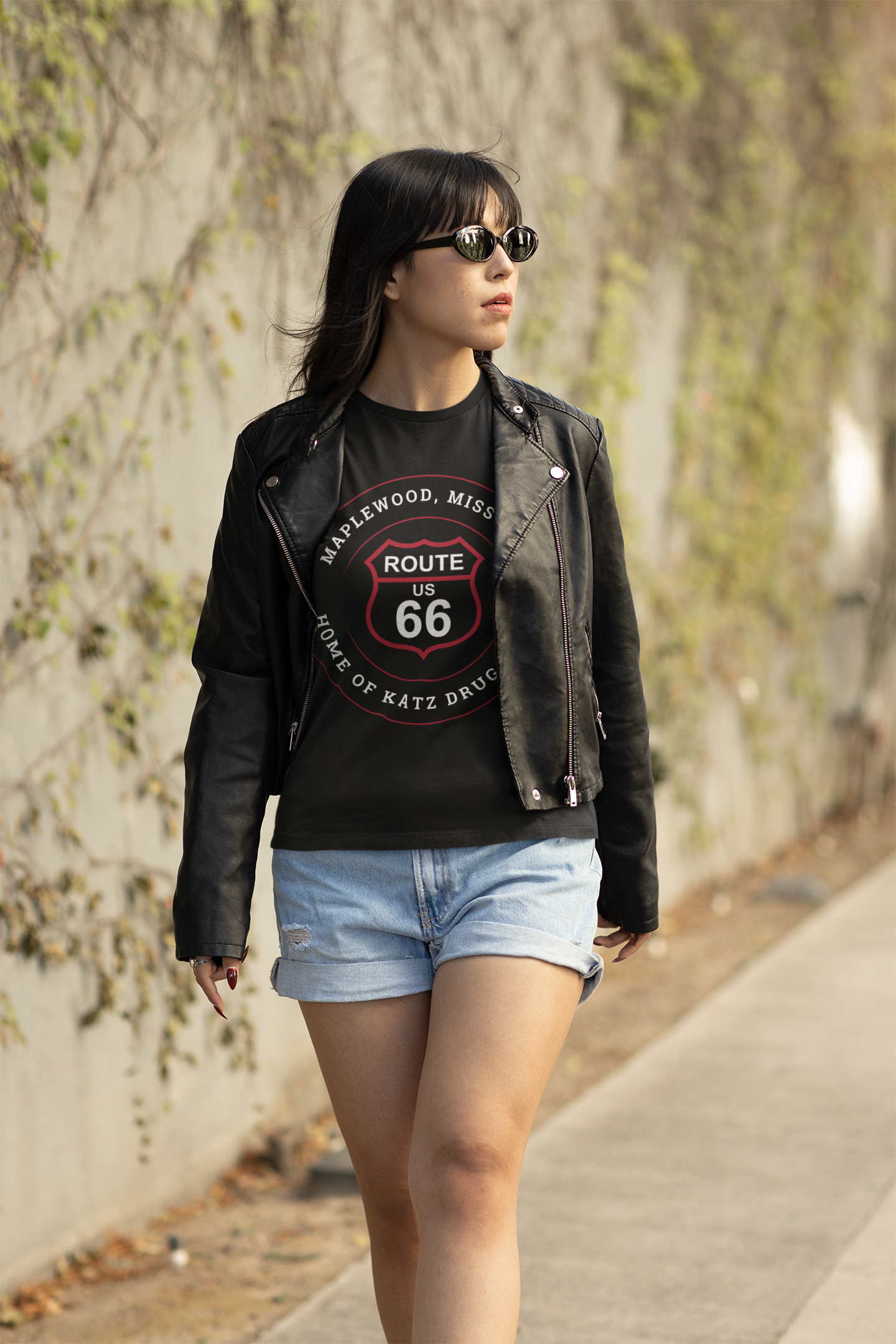 Female model wearing a black heather retro Route 66 unisex jersey tee with a Maplewood, MO: "Home of Katz Drugstore" design