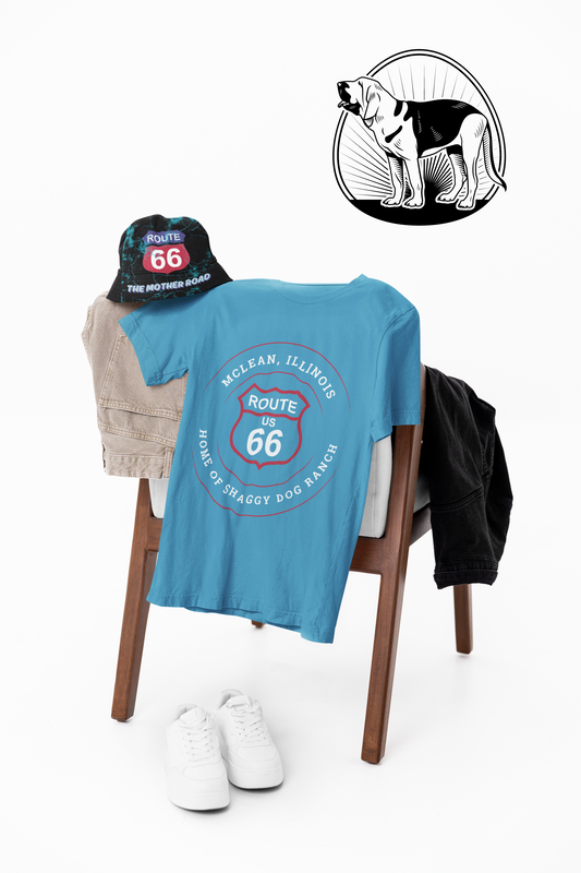 An aqua retro Route 66 unisex jersey tee with a McLean, IL: "Home of the Shaggy Dog Ranch" design is displayed hanging on a wooden chair along with a Route 66 bucket hat