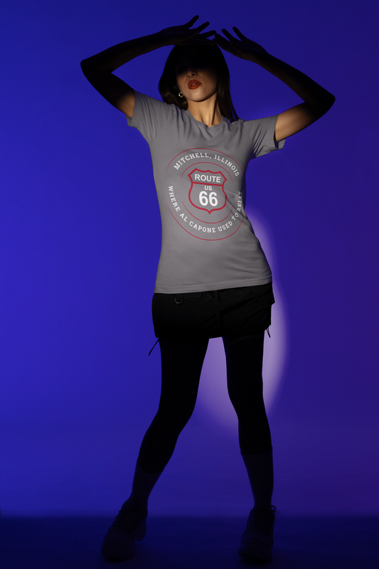 Female model wearing a grey retro Route 66 unisex jersey tee with a Mitchell, IL:: "Where Al Capone Used to Relax" design