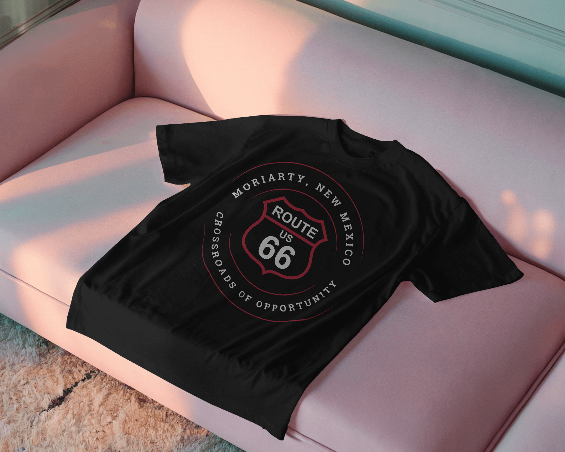 Black retro Route 66 unisex jersey tee with Moriarty, NM: "Crossroads of Opportunity" design displayed on a pink couch.