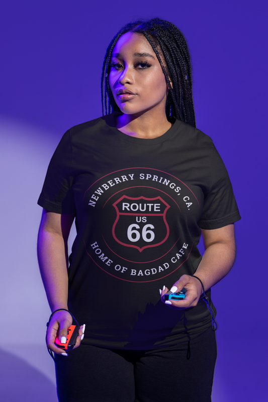 Female model wearing a black retro Route 66 unisex jersey tee with Newberry Springs, CA: "Home of Bagdad Cafe" design