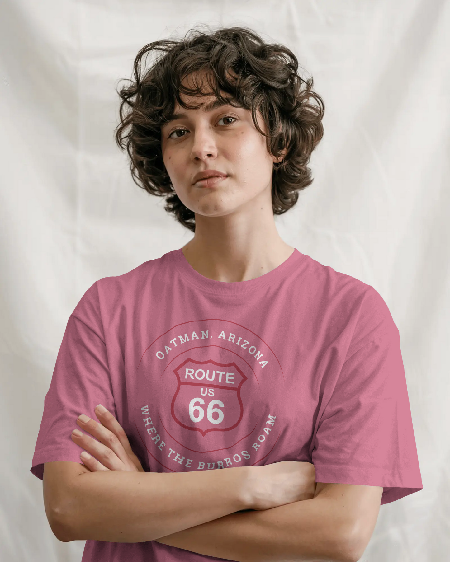 Cute female model with arms crossed and is wearing heather raspberry retro Route 66 unisex jersey tee with Oatman, AZ: "Where the Burros Roam" design