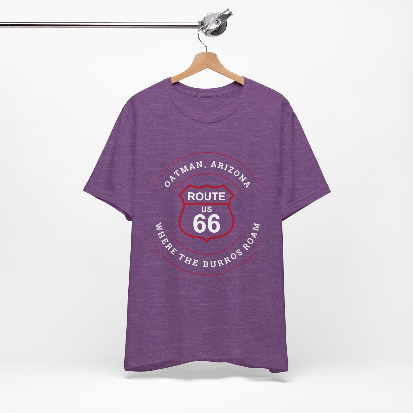 A heather team purple retro Route 66 unisex jersey tee with Oatman, AZ: "Where the Burros Roam" design hanging on a wooden hanger