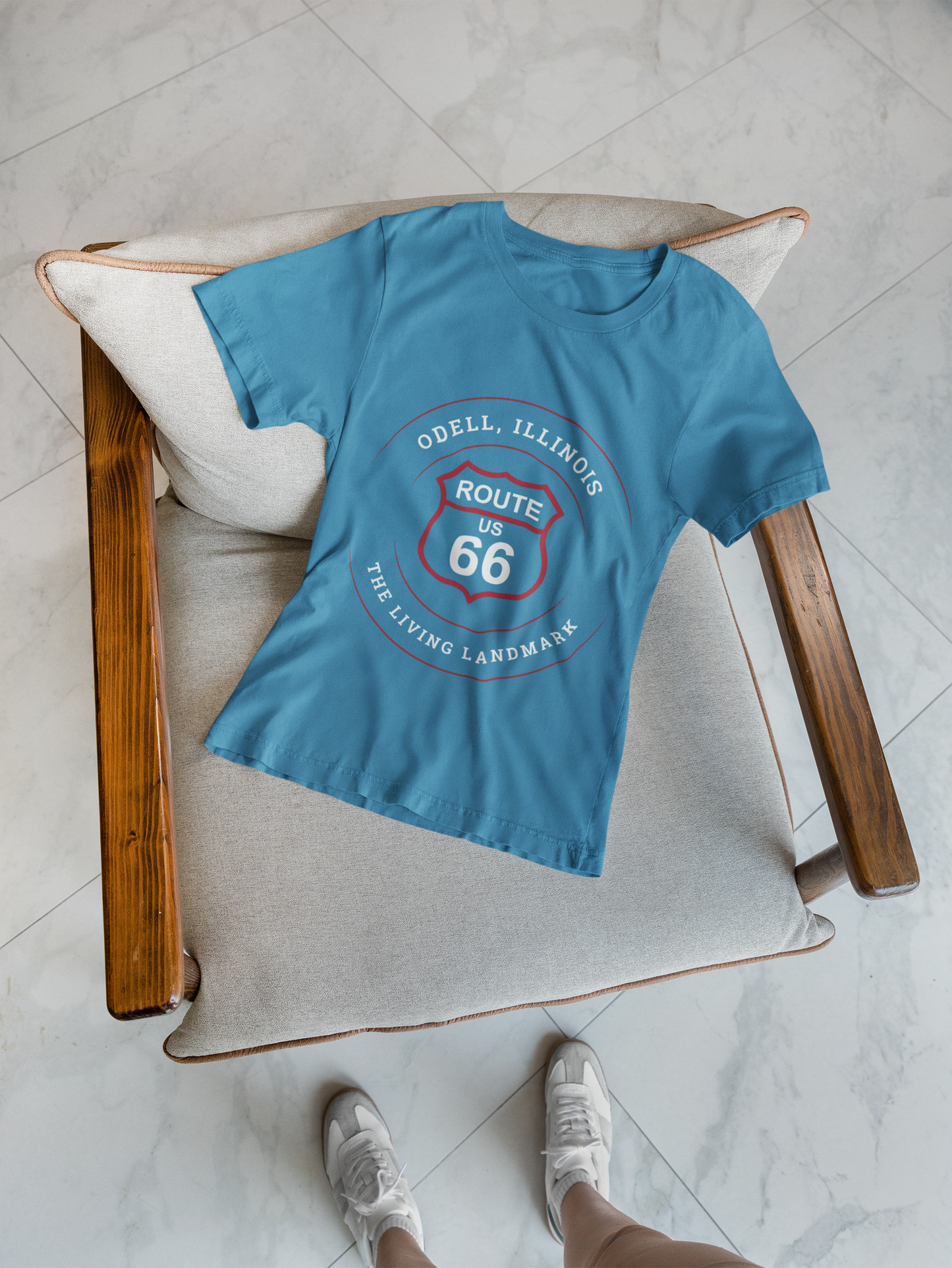 An aqua retro Route 66 unisex jersey tee with a Odell, IL: "The Living Landmark" design is displayed on a chair