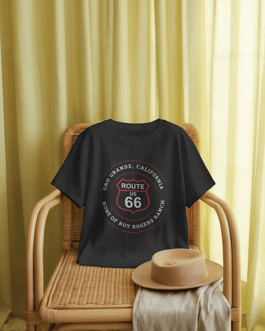 A black heather retro Route 66 unisex jersey tee with Oro Grande, CA: "Home of Roy Rogers Ranch" design is displayed on a wicker chair