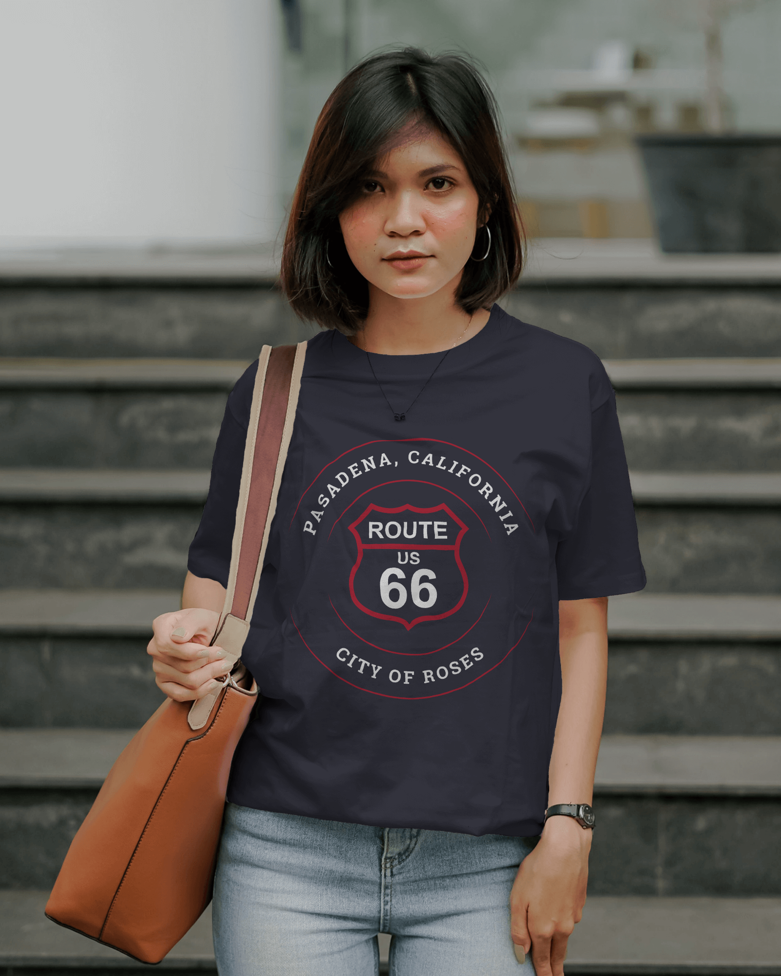 Female model with brown purse and wearing a black heather retro Route 66 unisex jersey tee with Pasadena, CA: "City of Roses"" design