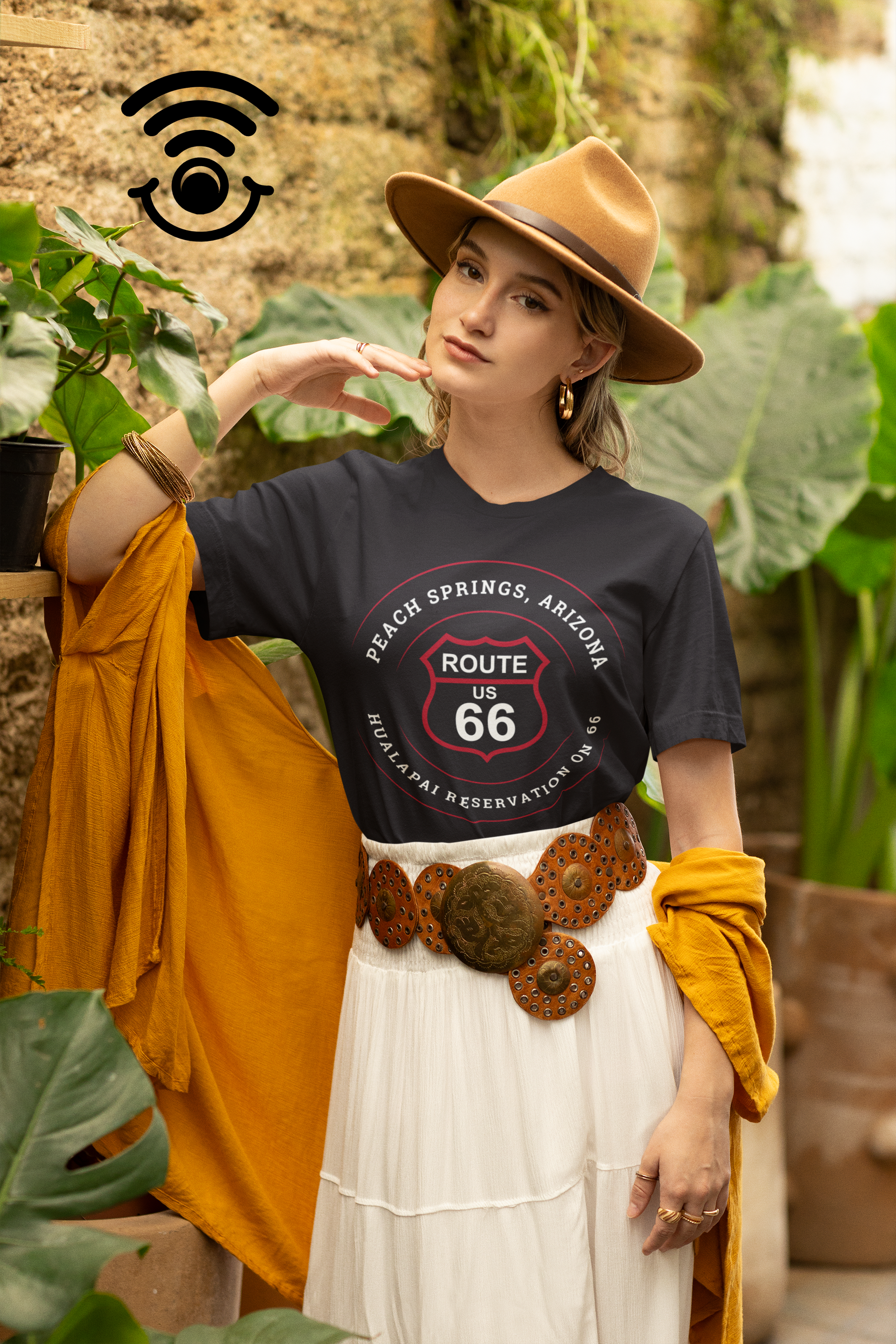 Female model wearing a fedora, a black retro Route 66 unisex jersey tee with Peach Springs, AZ: "Hualapai Reservation on 66" design and a western belt.