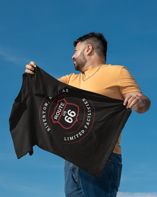 Male model holding a black heather retro Route 66 unisex jersey tee with Riverton, KS "Limited Facilities" design