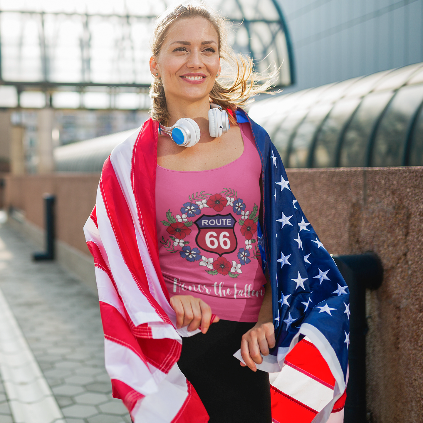 Smiling woman wearing a pink Route 66 "Honor the Fallen" tank top, draped in an American flag, perfect for Memorial Day or patriotic events
