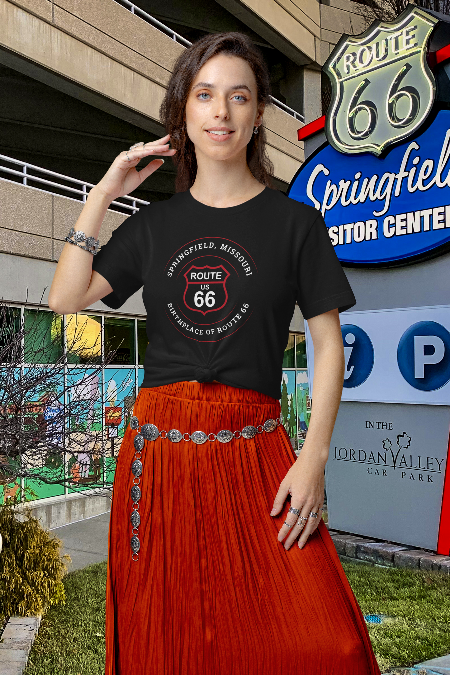 Female model wearing a black retro Route 66 unisex jersey tee with a Springfield, MO:: "Birthplace of Route 66" design as she stands by the Springfield Visitor Center