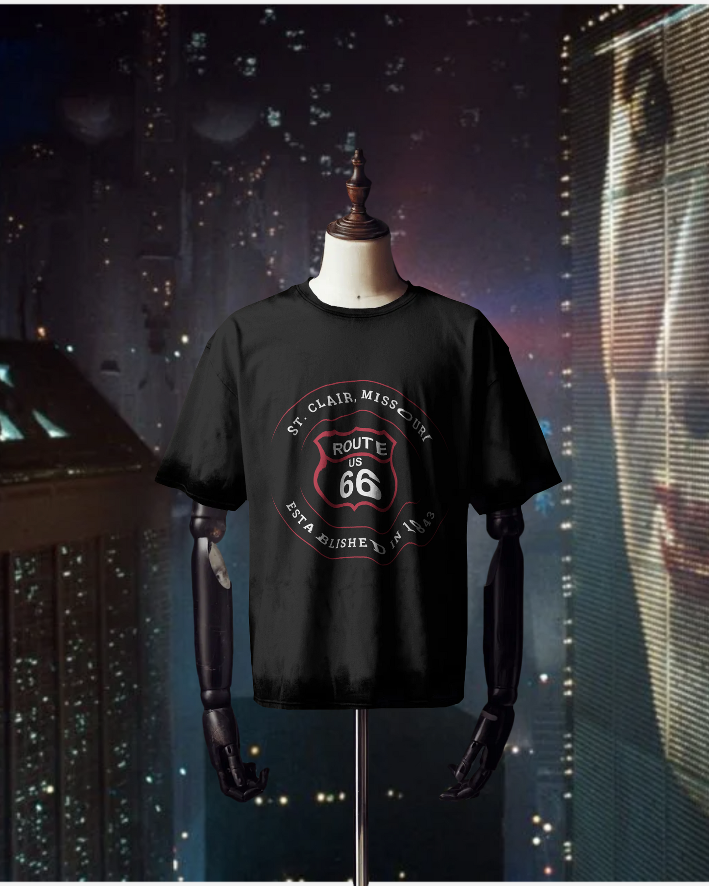 Mannequin wearing a black retro Route 66 unisex jersey tee with a St. Clair, MO: "Established in 1843" design. The mannequin is displayed in front of a wall-to-wall window where we see a dark, in-the-not-so-distant-future, Blade Runner-styled dystopian cityscape