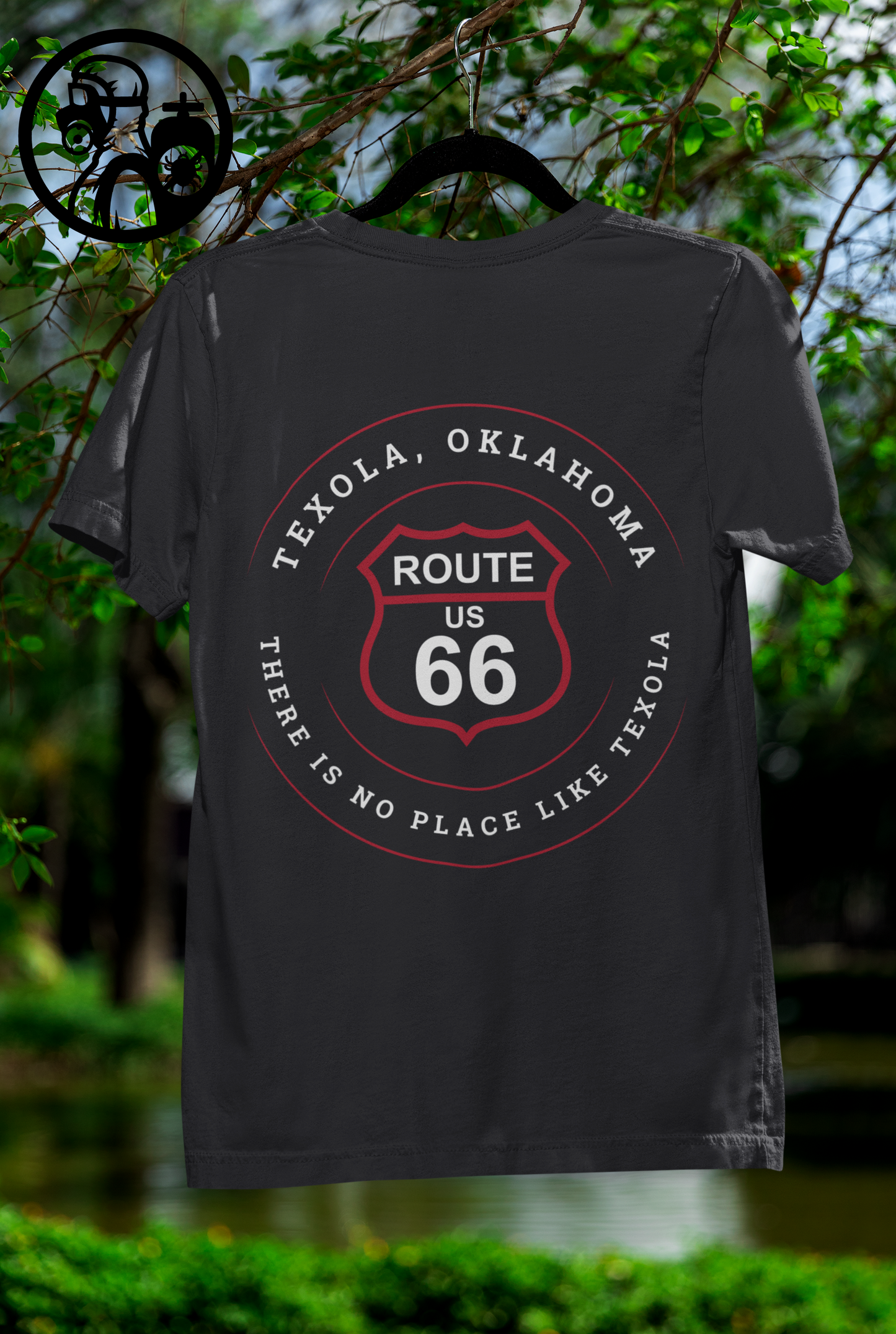 A vintage black retro Route 66 unisex jersey tee with Texola, OK: "There's No Place Like Texola" design displayed on a hanger which hangs from a tree branch
	